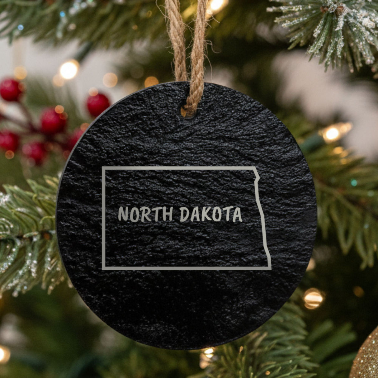 North Dakota round slate Christmas ornament engraved with the state outline and NORTH DAKOTA in hand-drawn brush lettering