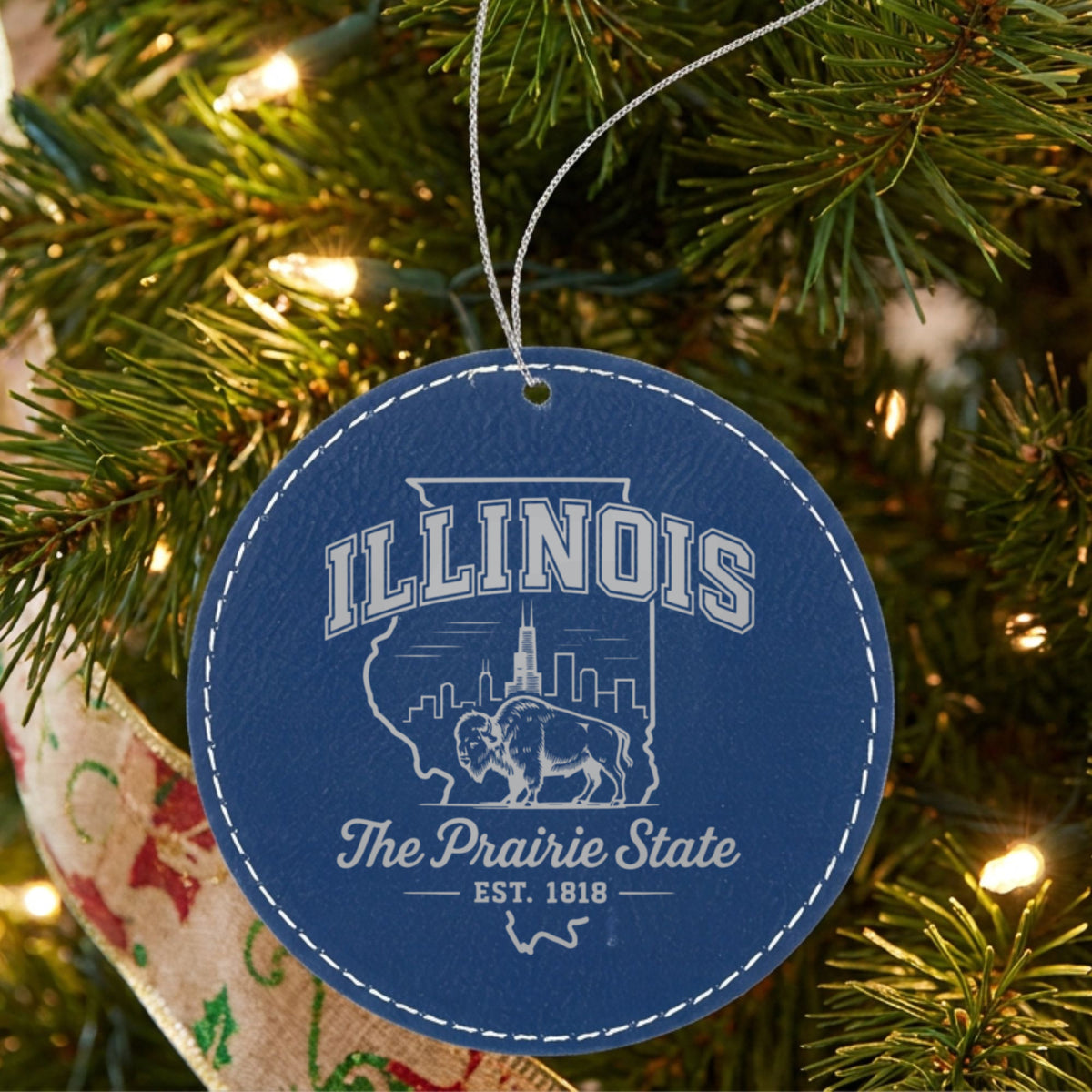 Blue leatherette round Christmas ornament laser engraved with an Illinois design of the Chicago skyline and a bison, hanging on a tree