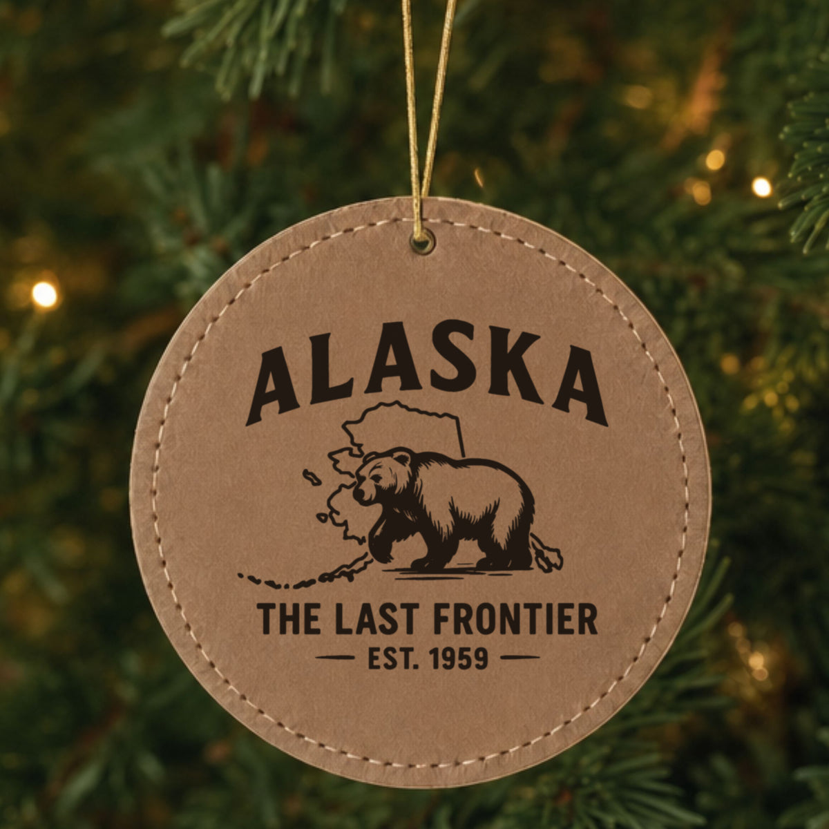 Brown leatherette round Christmas ornament laser engraved with an Alaska design of a grizzly bear crossing the state map, hanging on a tree