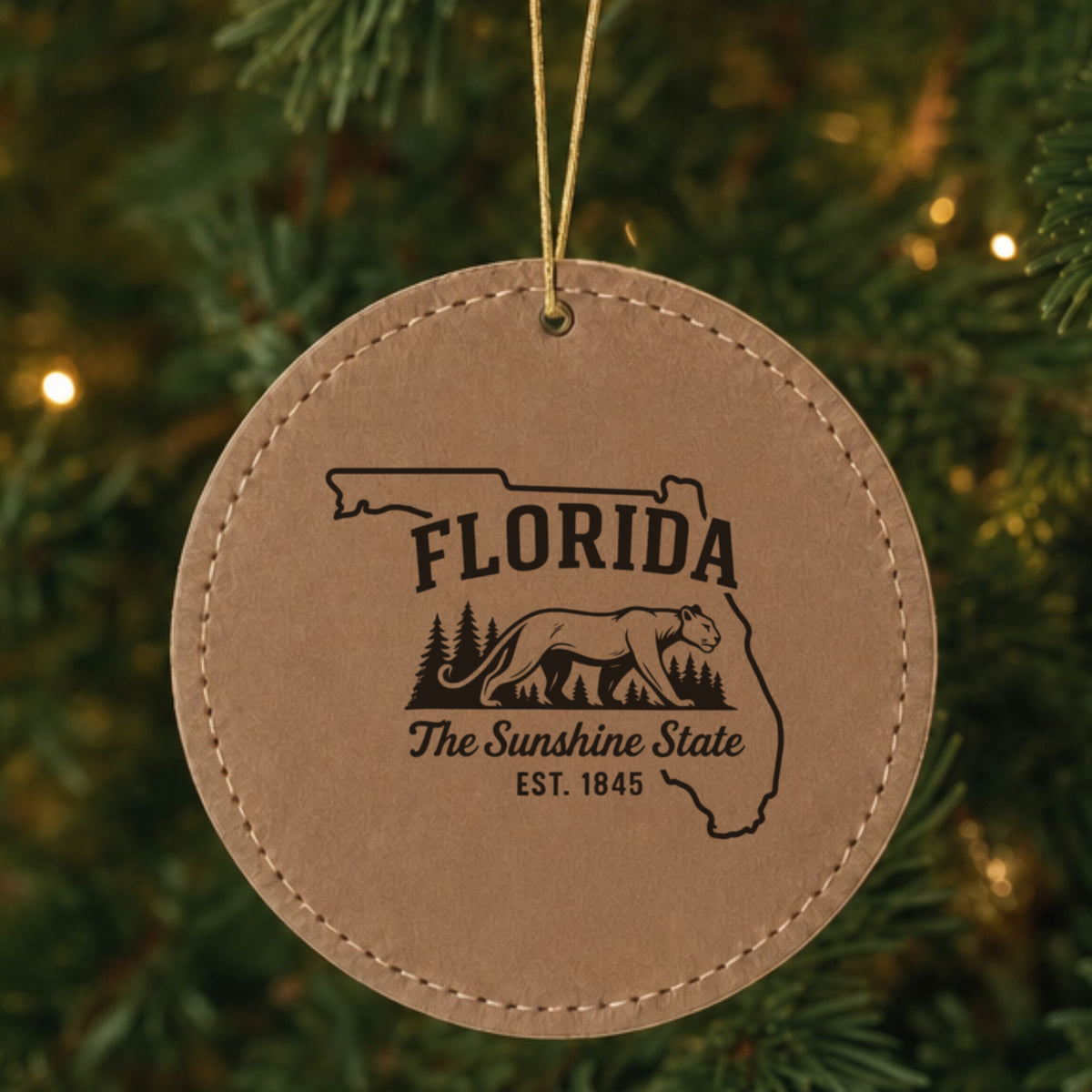 Brown leatherette round Christmas ornament laser engraved with a Florida design of a Florida panther and pine forest, hanging on a tree