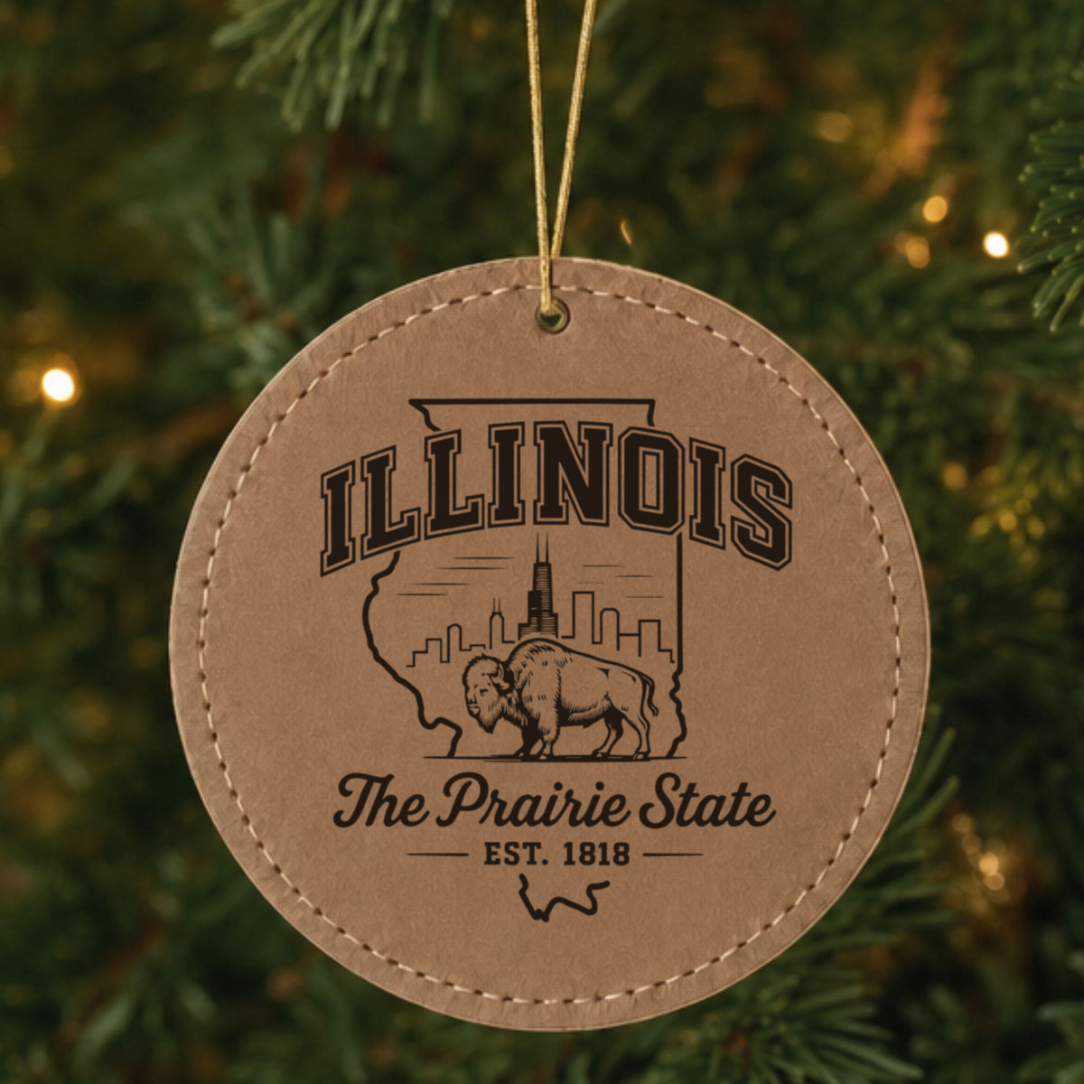 Brown leatherette round Christmas ornament laser engraved with an Illinois design of the Chicago skyline and a bison, hanging on a tree