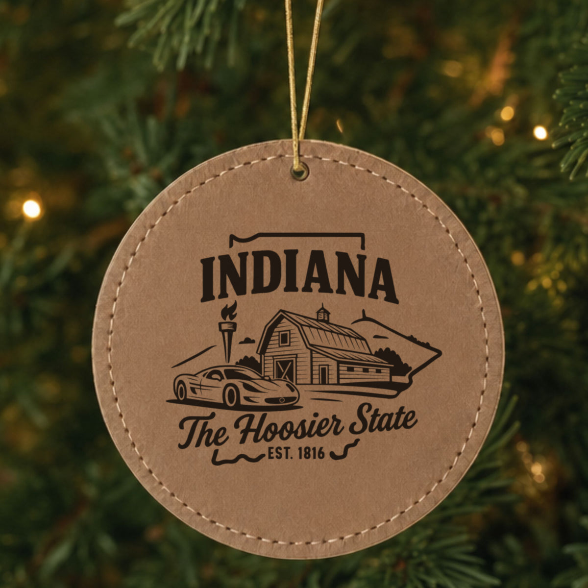 Brown leatherette round Christmas ornament laser engraved with an Indiana design of a red barn, a race car and a torch, hanging on a tree