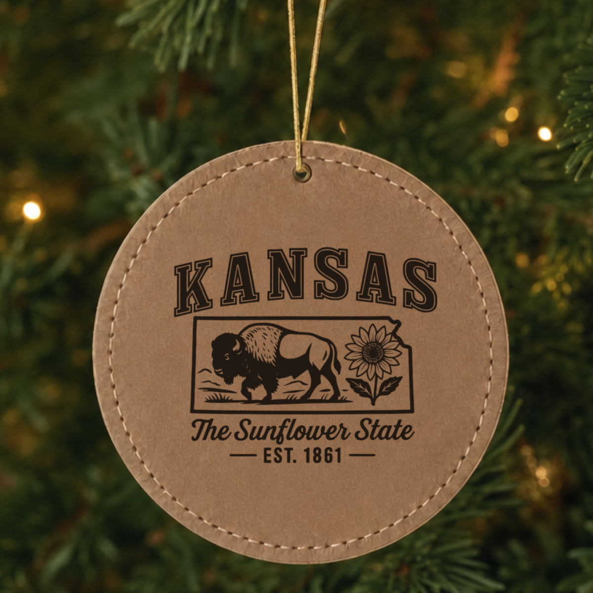Brown leatherette round Christmas ornament laser engraved with a Kansas design of a bison and a sunflower, hanging on a tree
