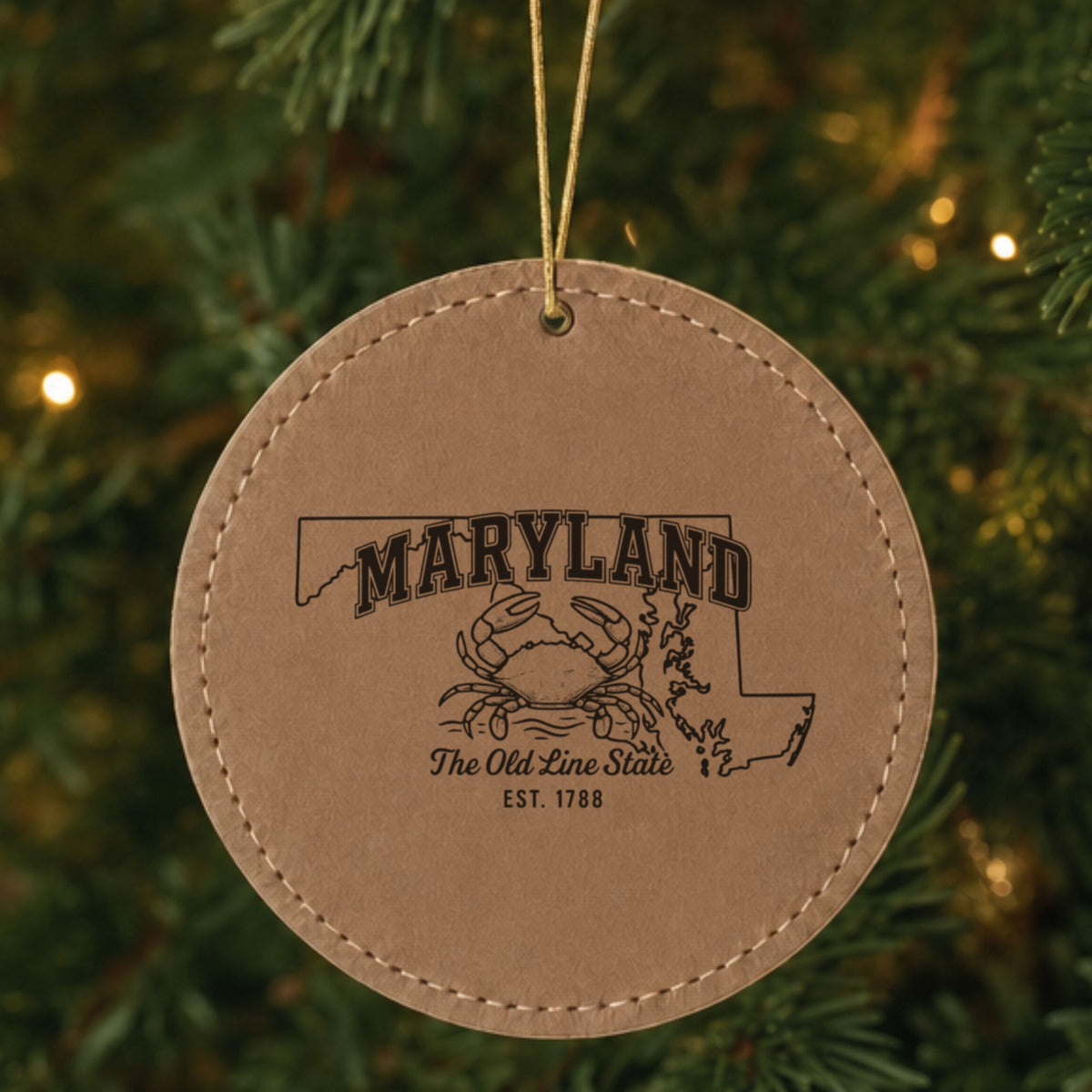 Brown leatherette round Christmas ornament laser engraved with a Maryland design of a blue crab on the Chesapeake, hanging on a tree
