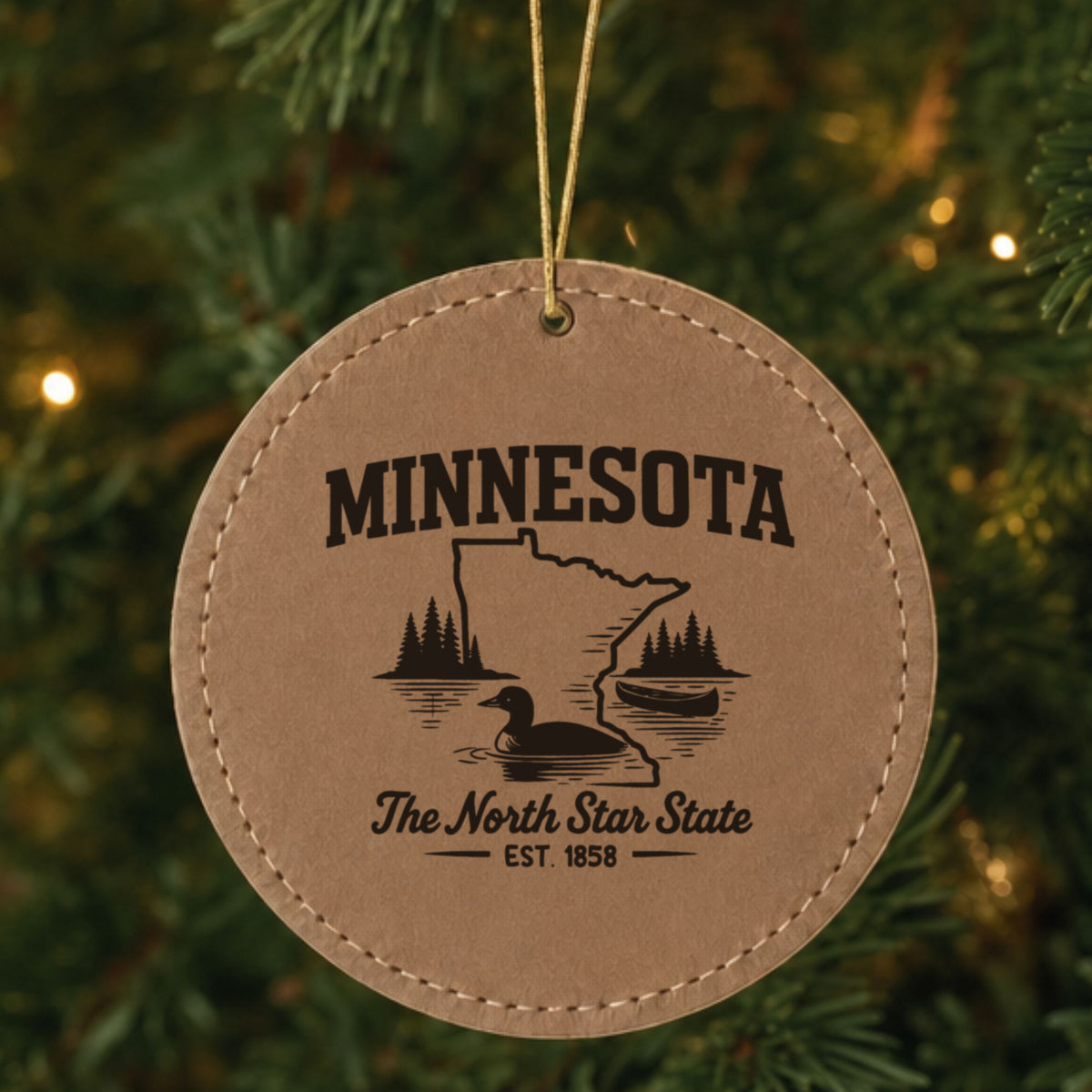 Brown leatherette round Christmas ornament laser engraved with a Minnesota design of a loon, a canoe and lakeside pines, hanging on a tree