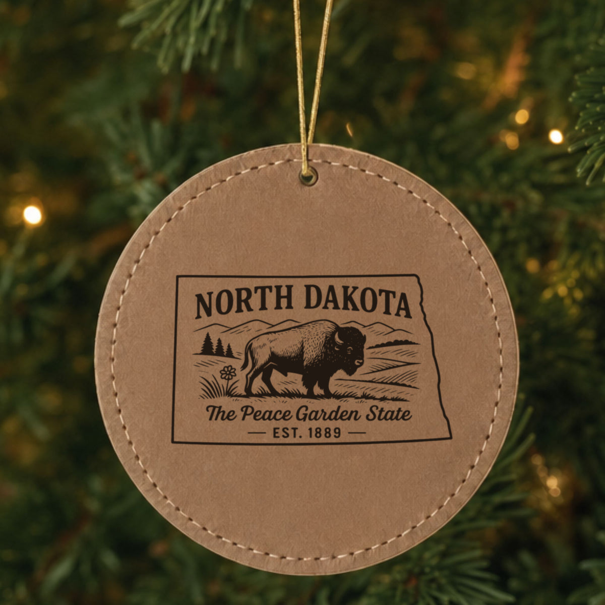 Brown leatherette round Christmas ornament laser engraved with a North Dakota design of a bison on the plains, hanging on a tree