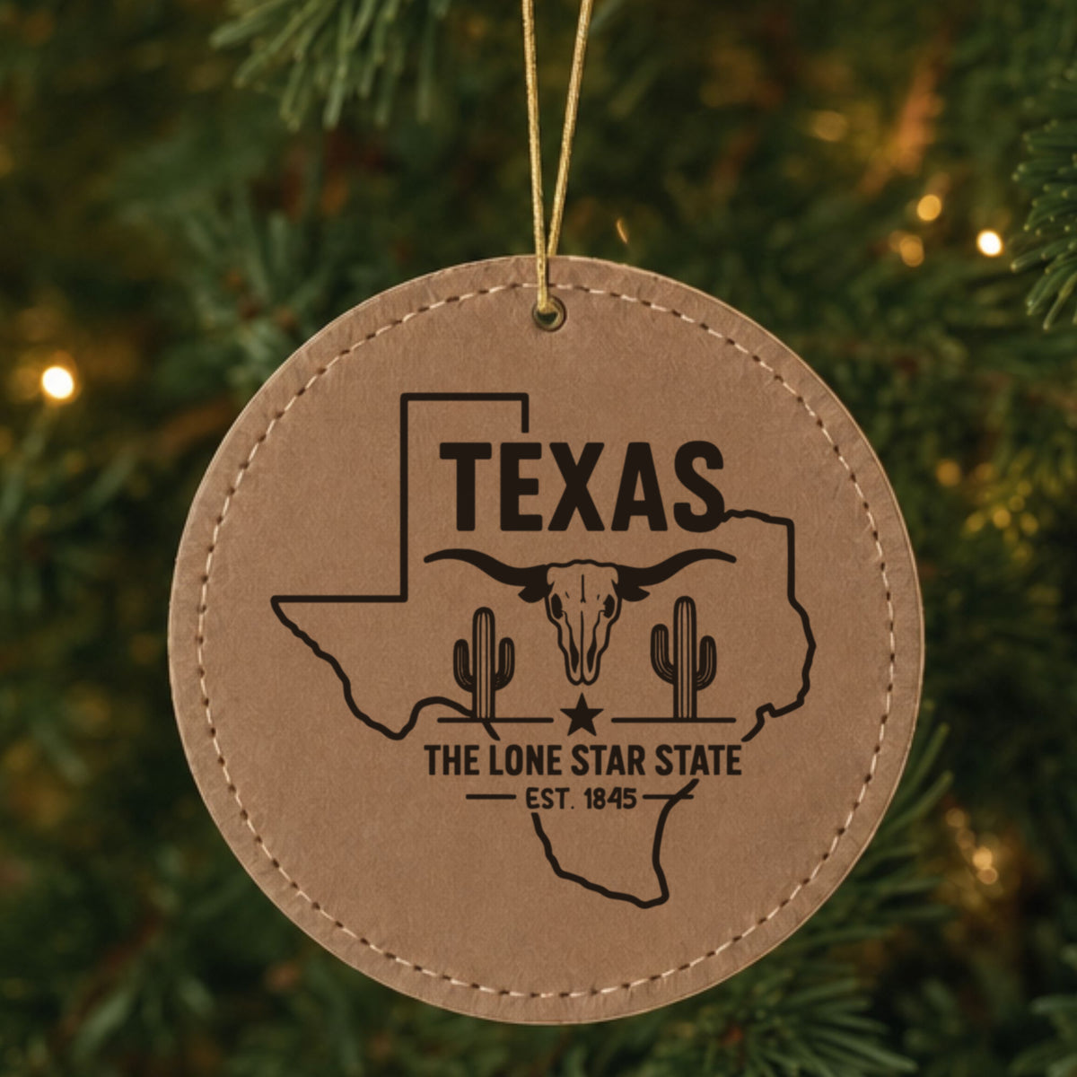 Brown leatherette round Christmas ornament laser engraved with a Texas design of a longhorn skull, cactus and a lone star, hanging on a tree