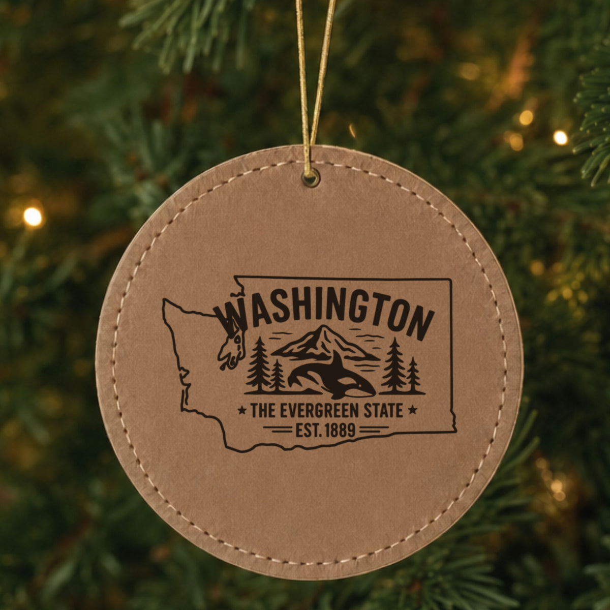Brown leatherette round Christmas ornament laser engraved with a Washington design of an orca, Mount Rainier and evergreens, hanging on a tree
