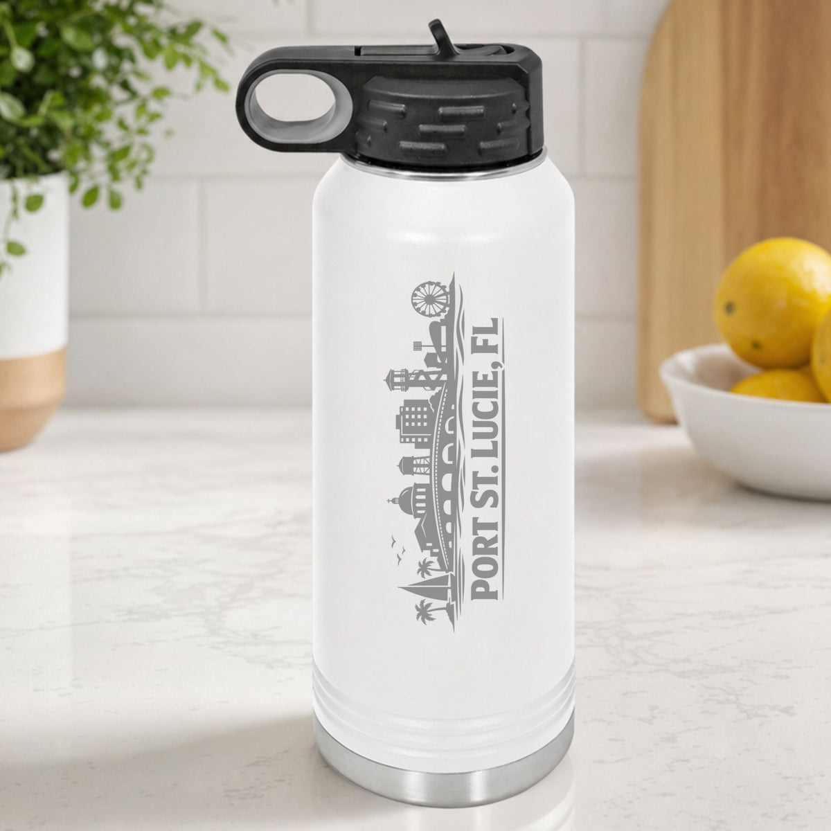 White 32 oz insulated water bottle laser engraved with the Port St. Lucie, Florida skyline running up the side, standing on a kitchen counter