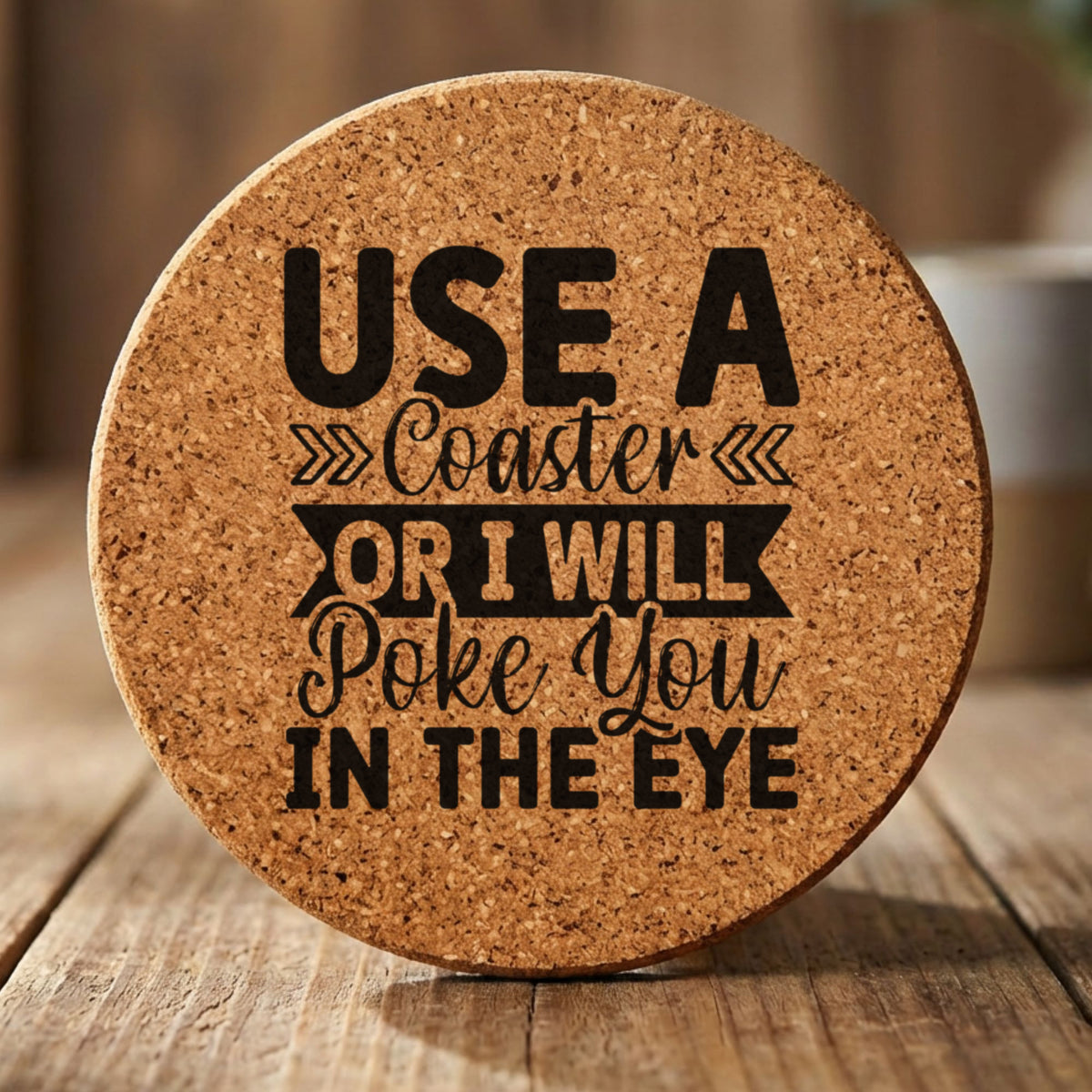 Round cork coaster laser engraved with "Use a Coaster or I Will Poke You in the Eye", hand lettered design