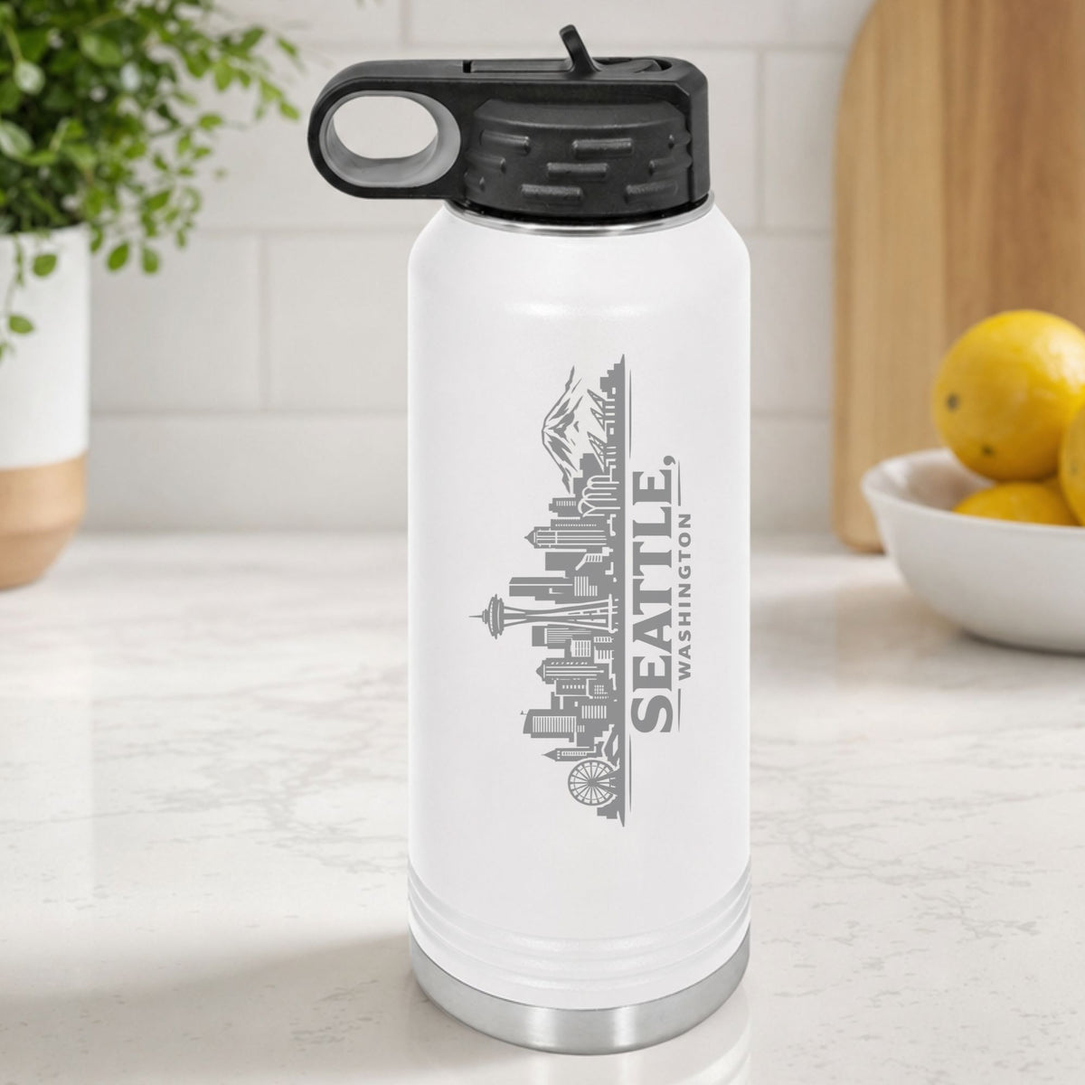 White 32 oz insulated water bottle laser engraved with the Seattle, Washington skyline running up the side, standing on a kitchen counter