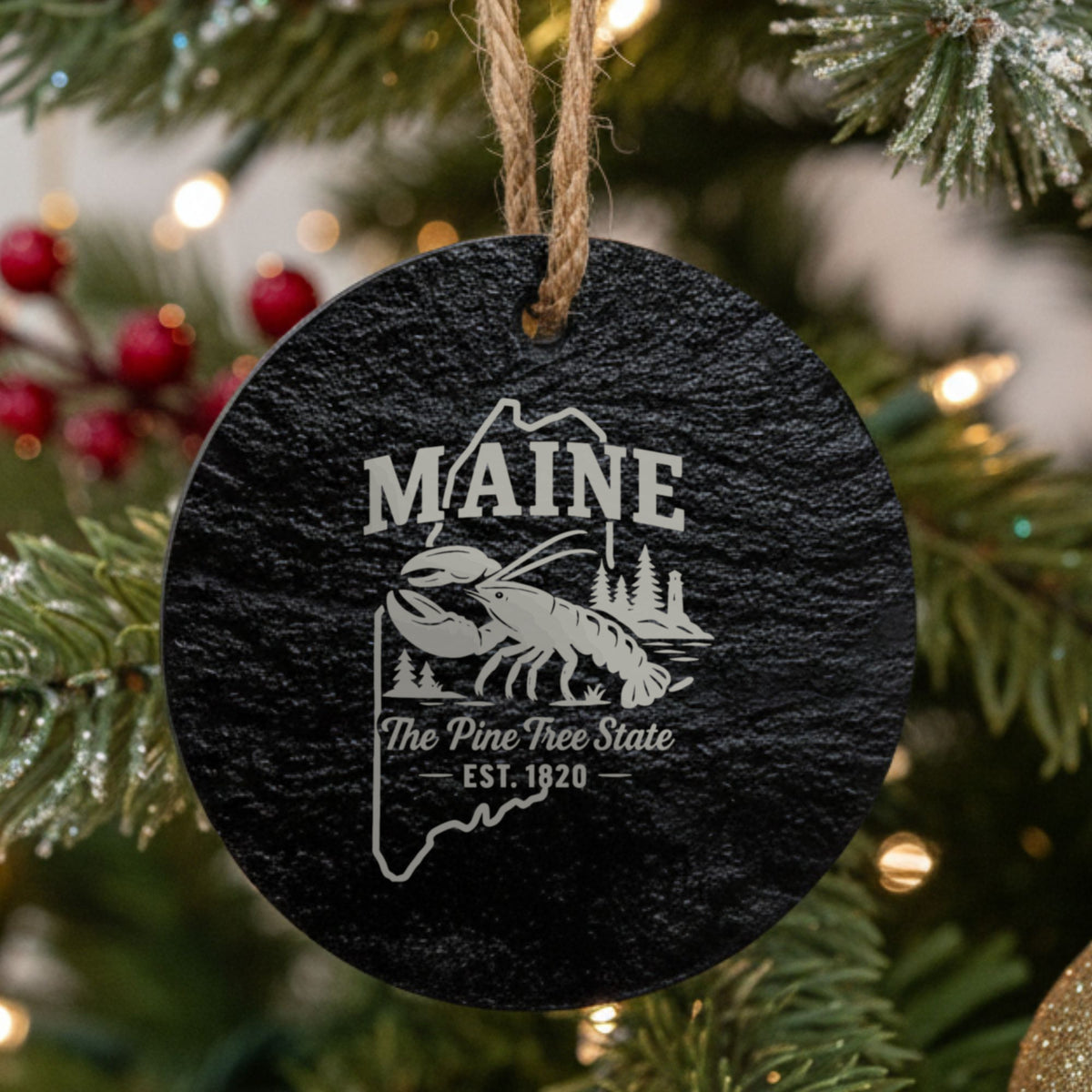 Round slate Christmas ornament laser engraved with a Maine design of a lobster, pines and a lighthouse