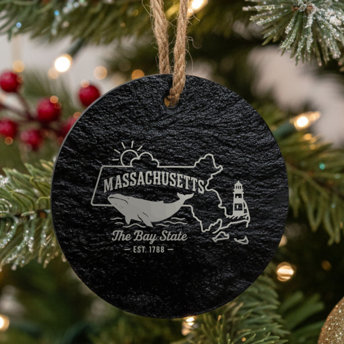 Round slate Christmas ornament laser engraved with a Massachusetts design of a whale, a lighthouse and the sun over Cape Cod and the islands