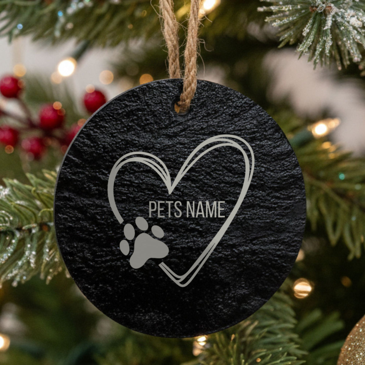 Round slate Christmas ornament engraved with a sketched heart and a paw print, showing where your pet's name goes