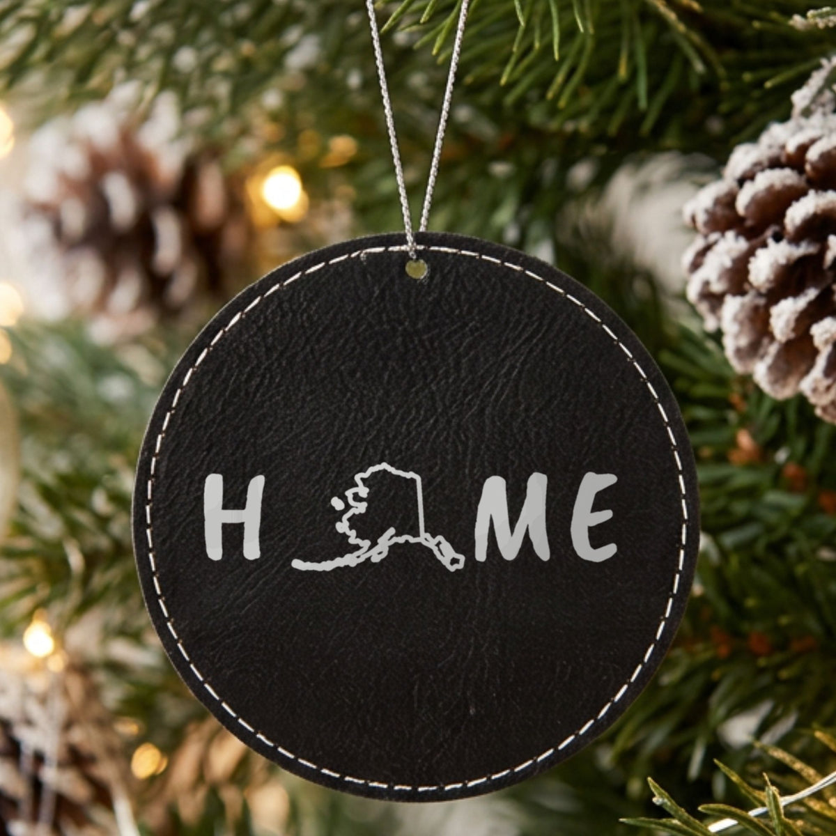Black leatherette round Christmas ornament laser engraved with the Alaska HOME Outline design, hanging on a tree