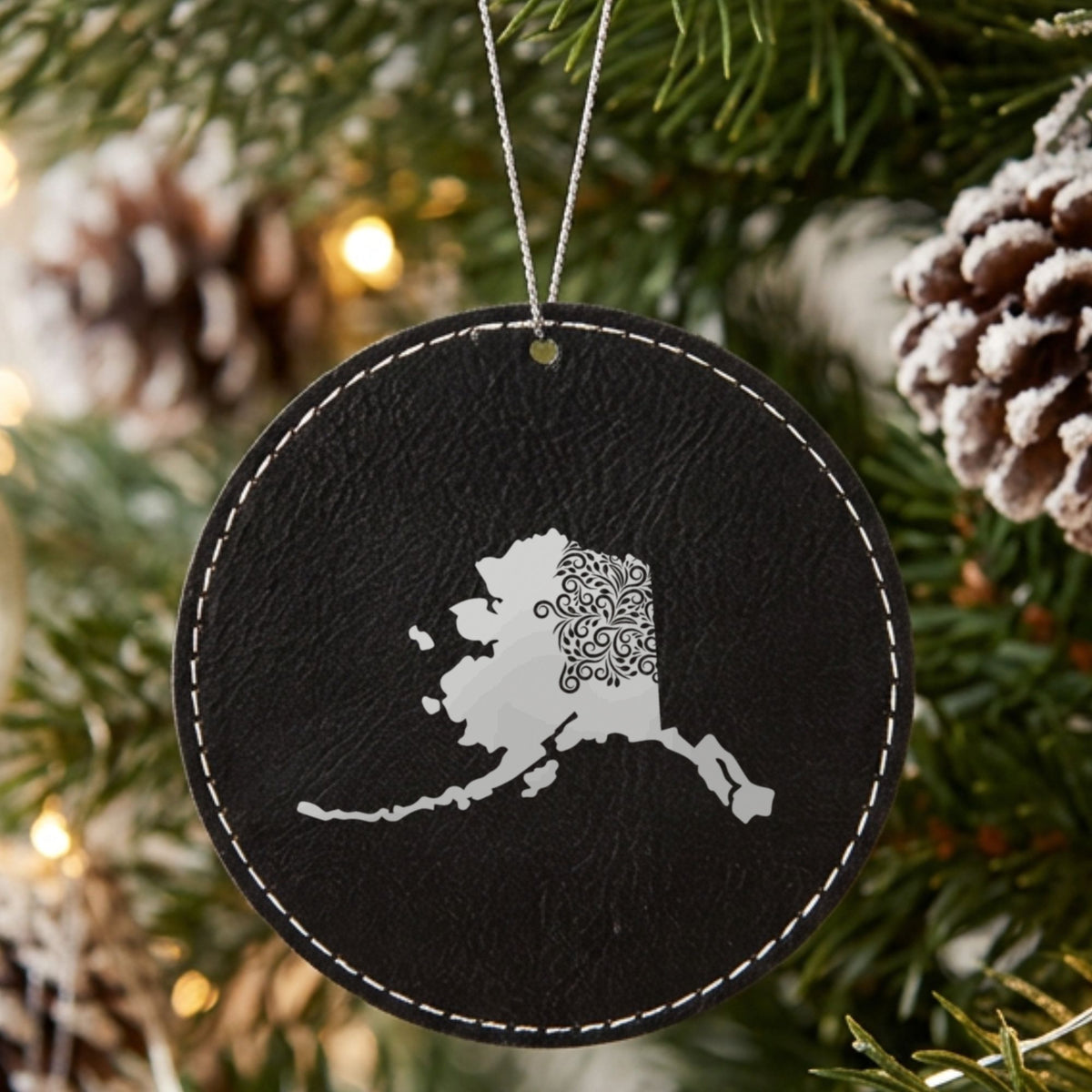 Black leatherette round Christmas ornament laser engraved with the Alaska Floral Damask design, hanging on a tree
