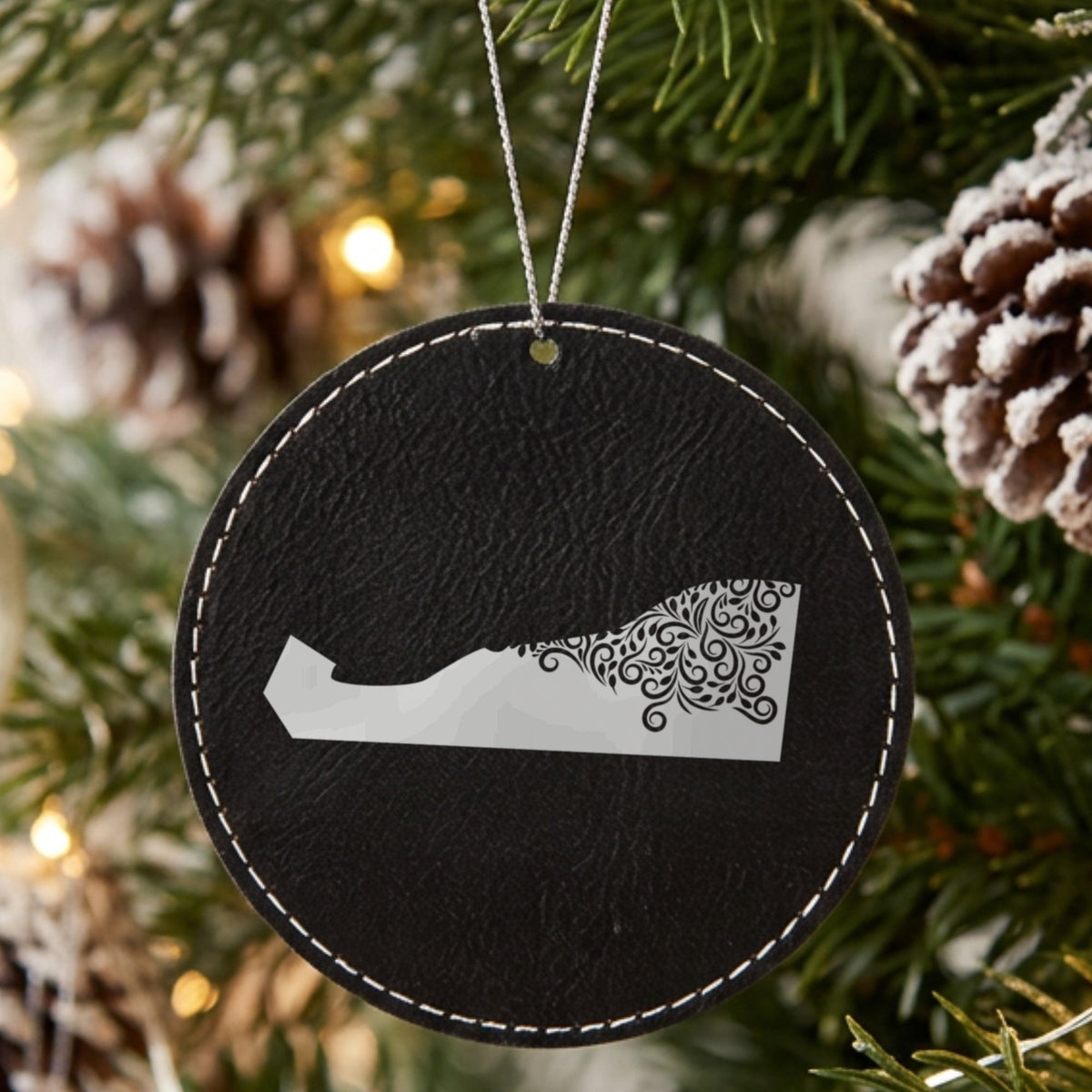 Black leatherette round Christmas ornament laser engraved with the Delaware Floral Damask design, hanging on a tree