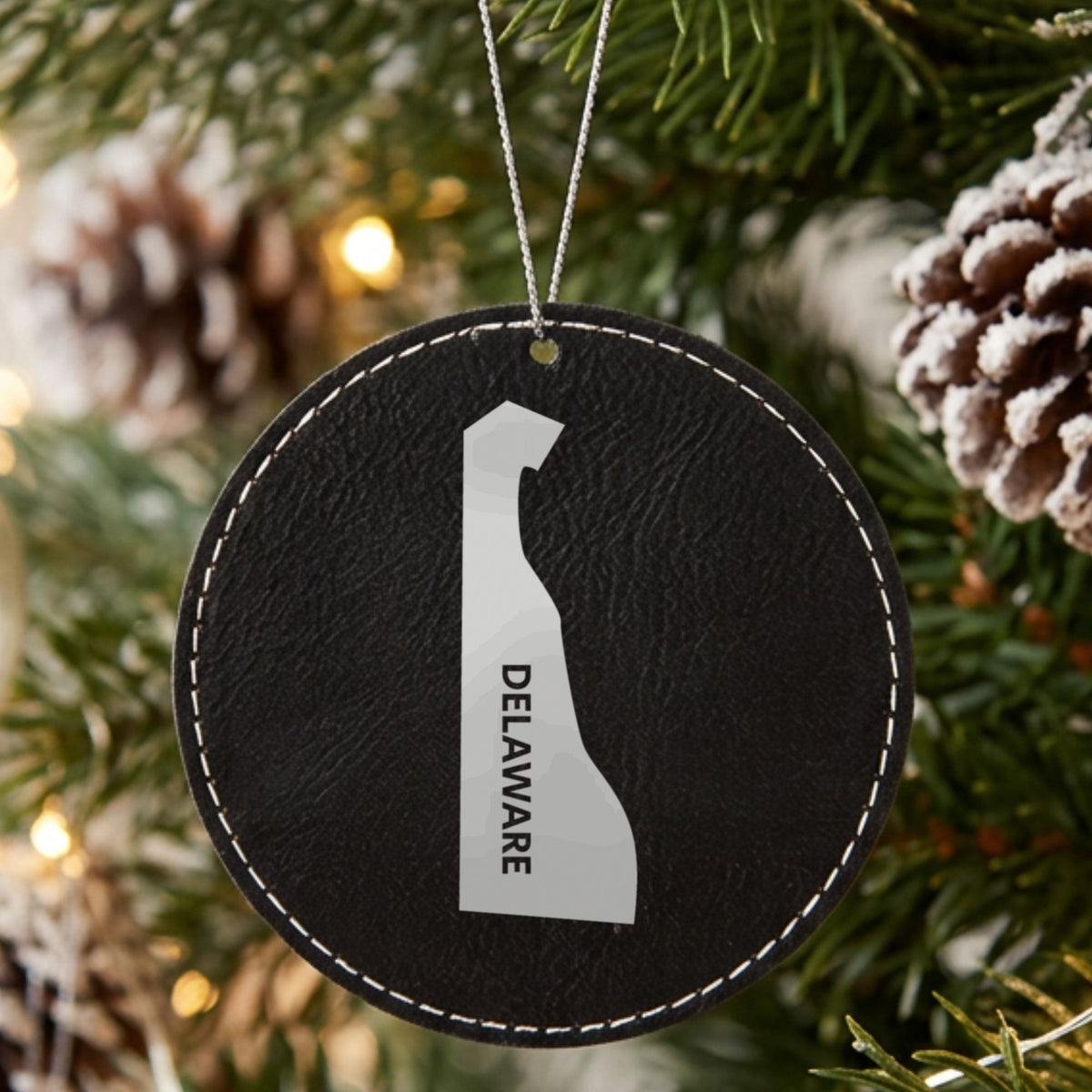 Black leatherette round Christmas ornament laser engraved with the Delaware Vertical Name (Engraved) design, hanging on a tree