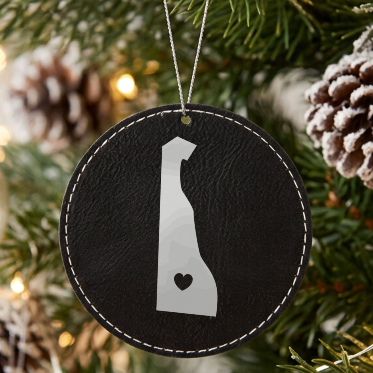 Black leatherette round Christmas ornament laser engraved with the Delaware Heart Accent design, hanging on a tree
