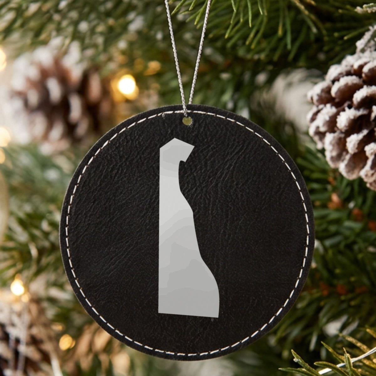 Black leatherette round Christmas ornament laser engraved with the Delaware Engraved State design, hanging on a tree