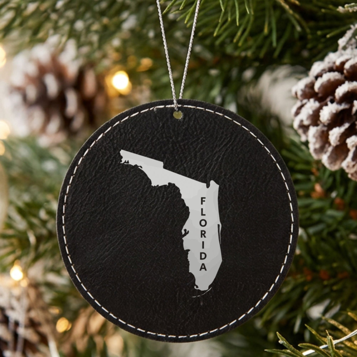 Black leatherette round Christmas ornament laser engraved with the Florida Vertical Name (Engraved) design, hanging on a tree
