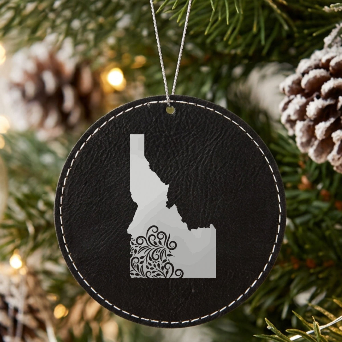 Black leatherette round Christmas ornament laser engraved with the Idaho Floral Damask design, hanging on a tree