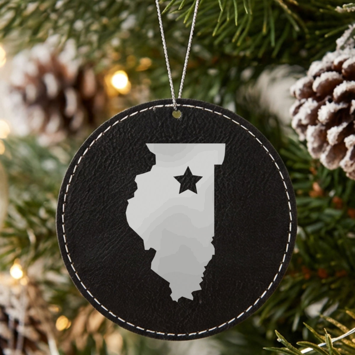 Black leatherette round Christmas ornament laser engraved with the Illinois Star Accent design, hanging on a tree