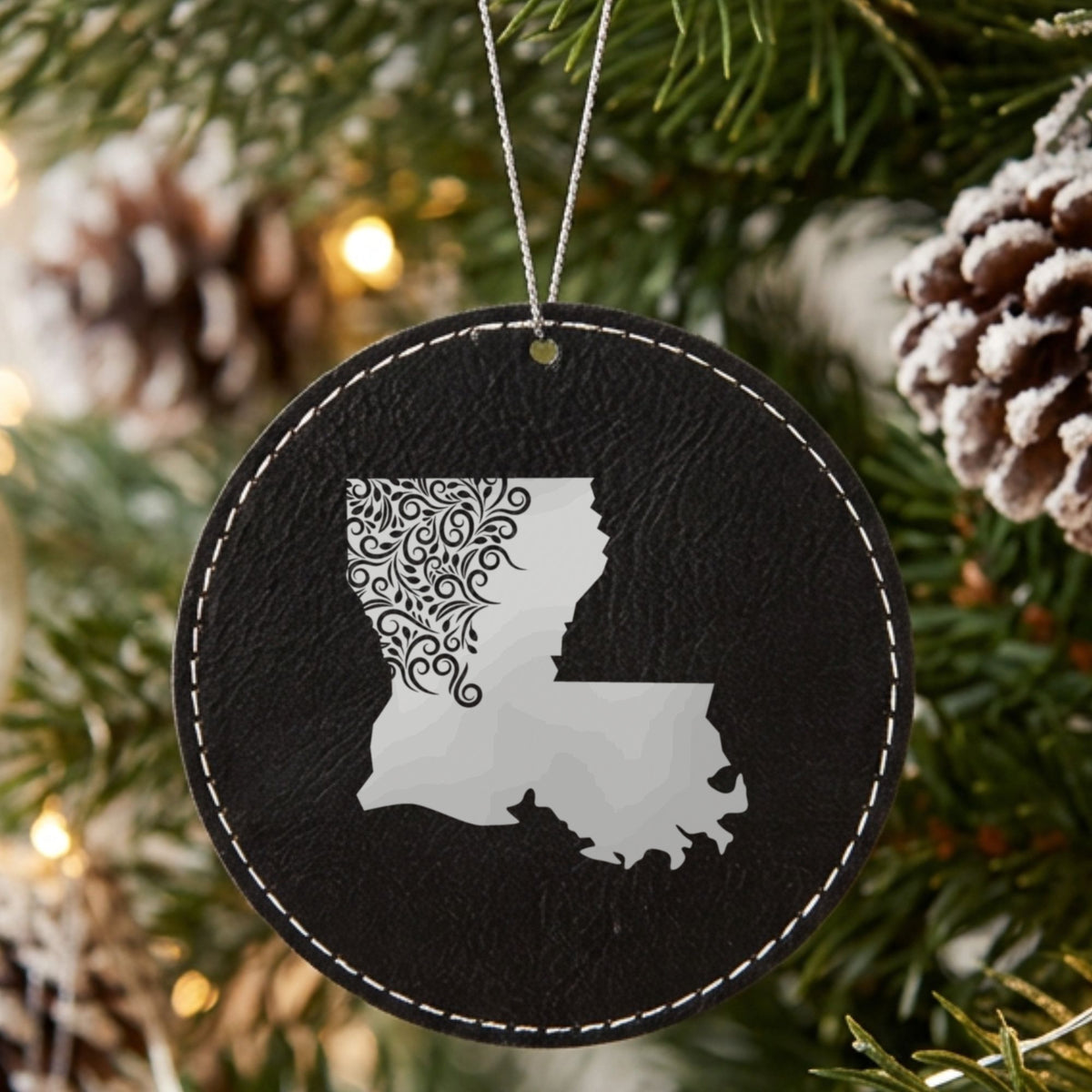 Black leatherette round Christmas ornament laser engraved with the Louisiana Floral Damask design, hanging on a tree