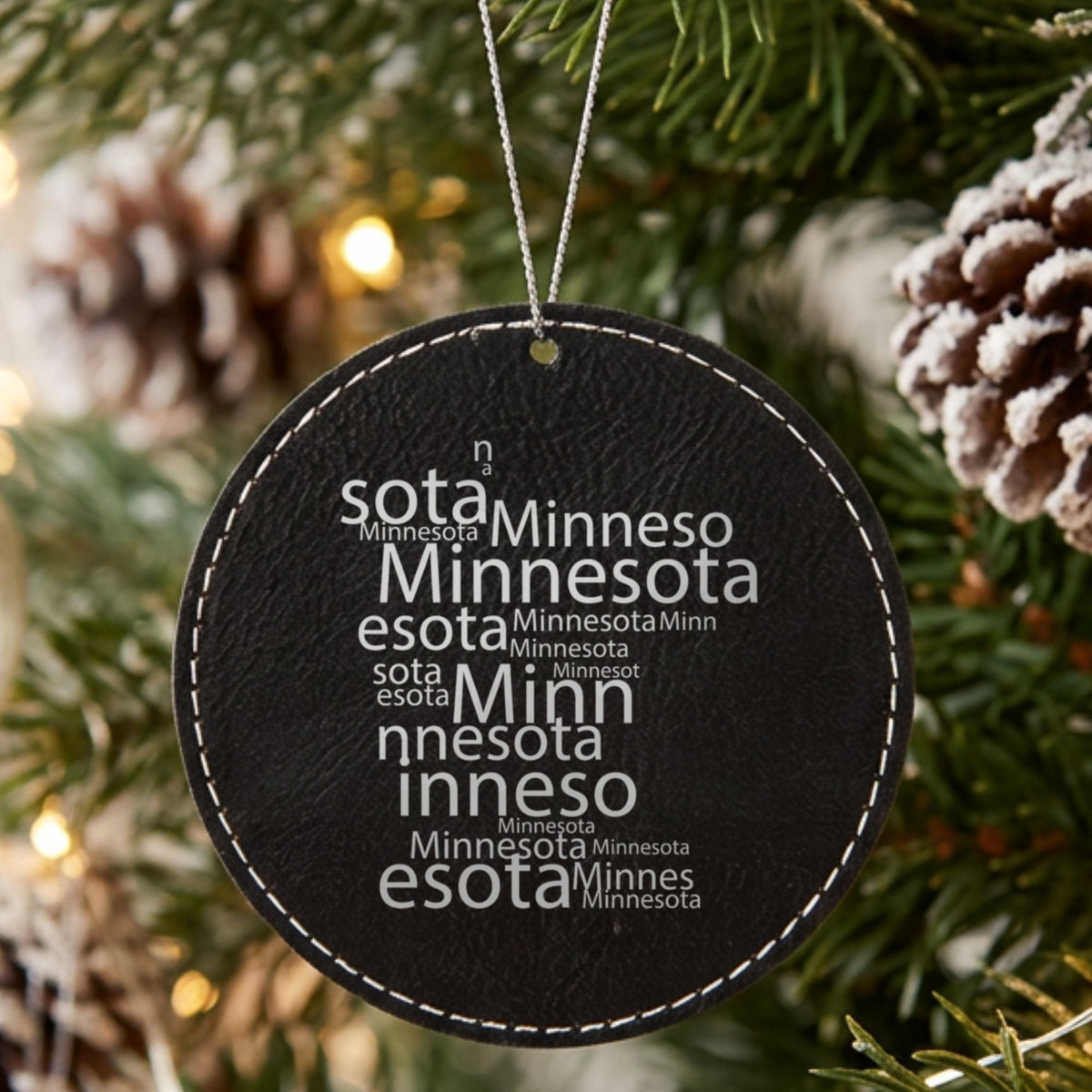 Black leatherette round Christmas ornament laser engraved with the Minnesota Word Cloud design, hanging on a tree