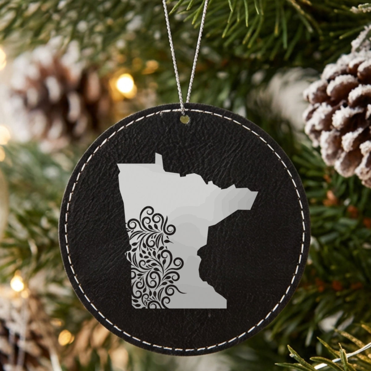 Black leatherette round Christmas ornament laser engraved with the Minnesota Floral Damask design, hanging on a tree