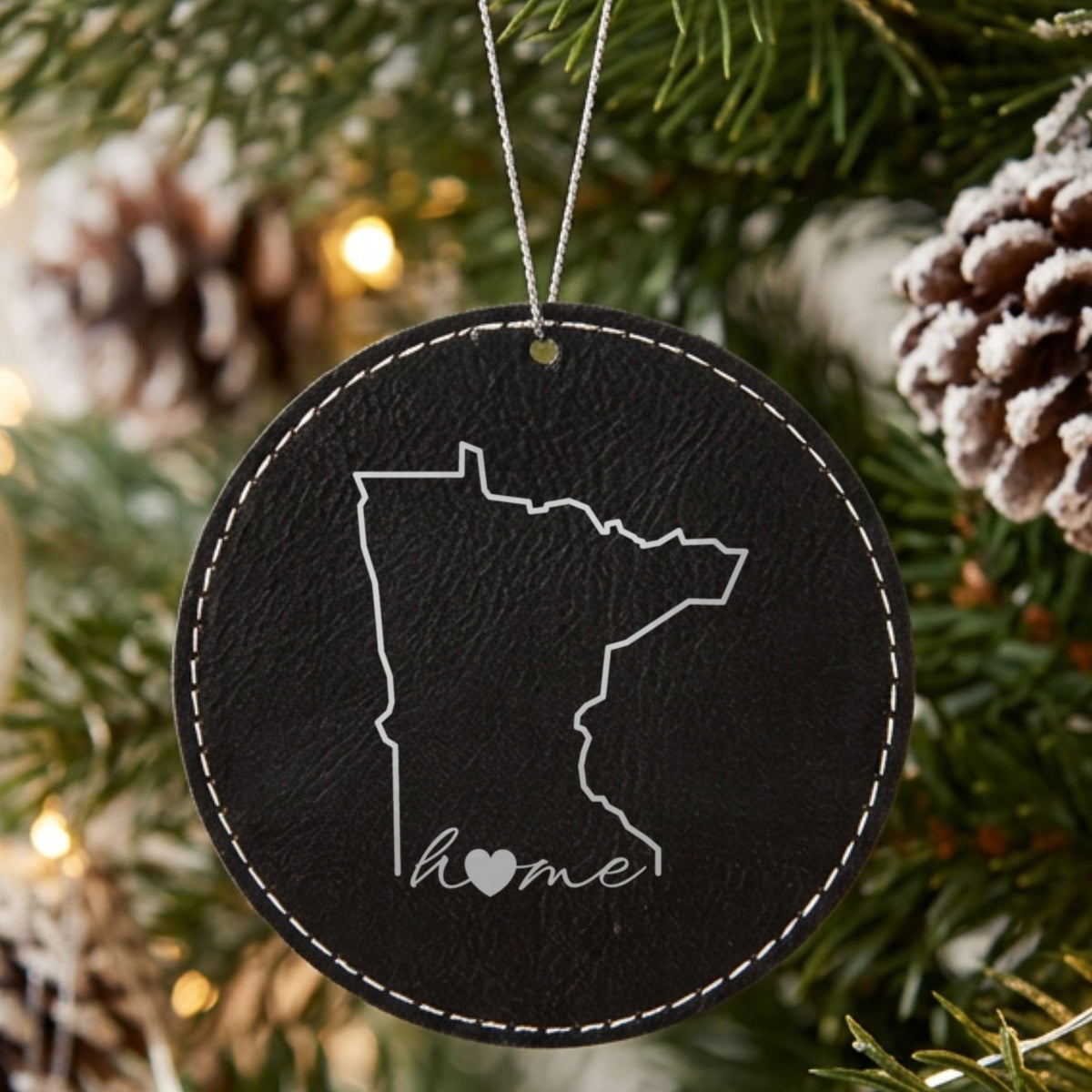 Black leatherette round Christmas ornament laser engraved with the Minnesota Home Script & Heart design, hanging on a tree