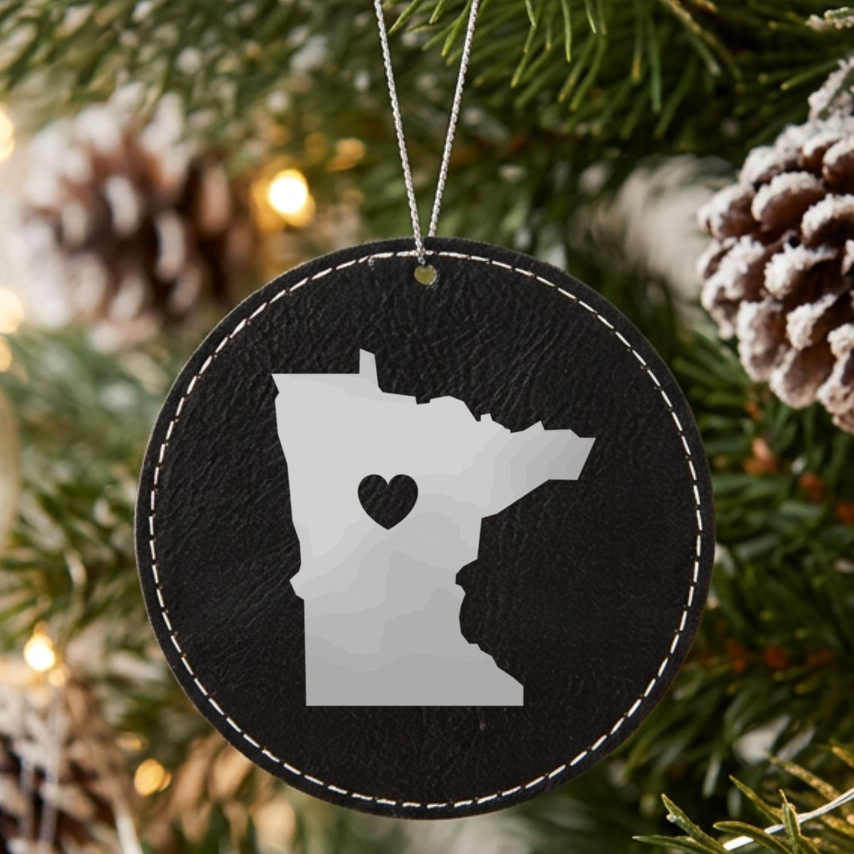 Black leatherette round Christmas ornament laser engraved with the Minnesota Heart Accent design, hanging on a tree