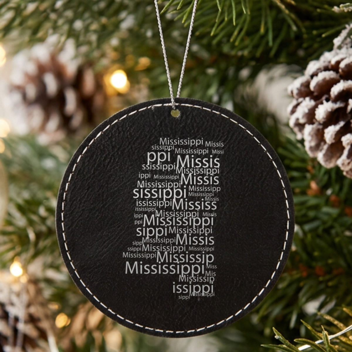 Black leatherette round Christmas ornament laser engraved with the Mississippi Word Cloud design, hanging on a tree
