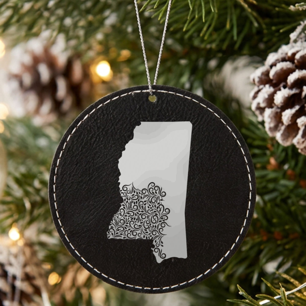 Black leatherette round Christmas ornament laser engraved with the Mississippi Floral Damask design, hanging on a tree