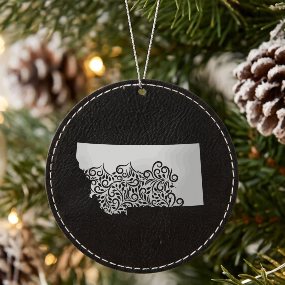 Black leatherette round Christmas ornament laser engraved with the Montana Floral Damask design, hanging on a tree