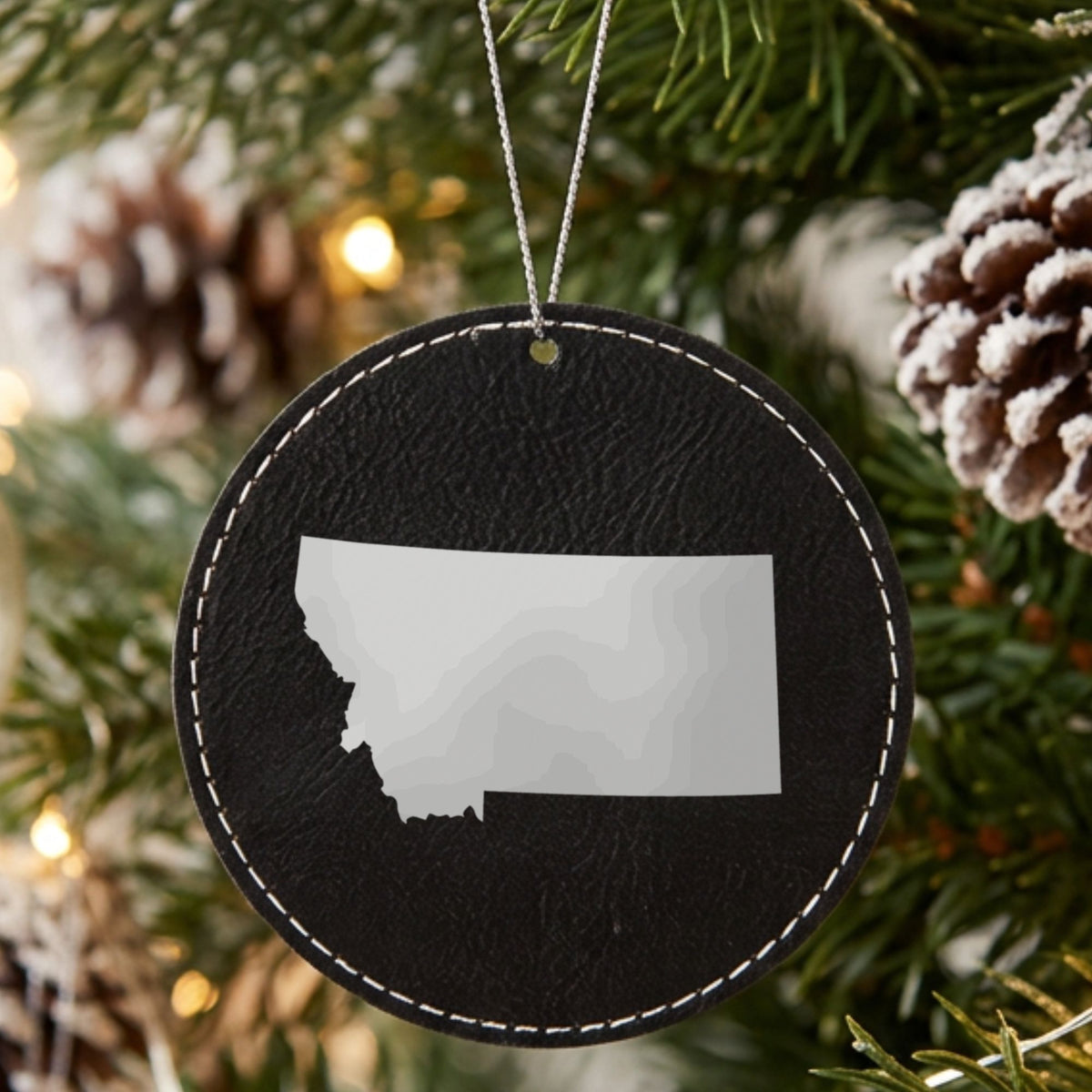 Black leatherette round Christmas ornament laser engraved with the Montana Engraved State design, hanging on a tree