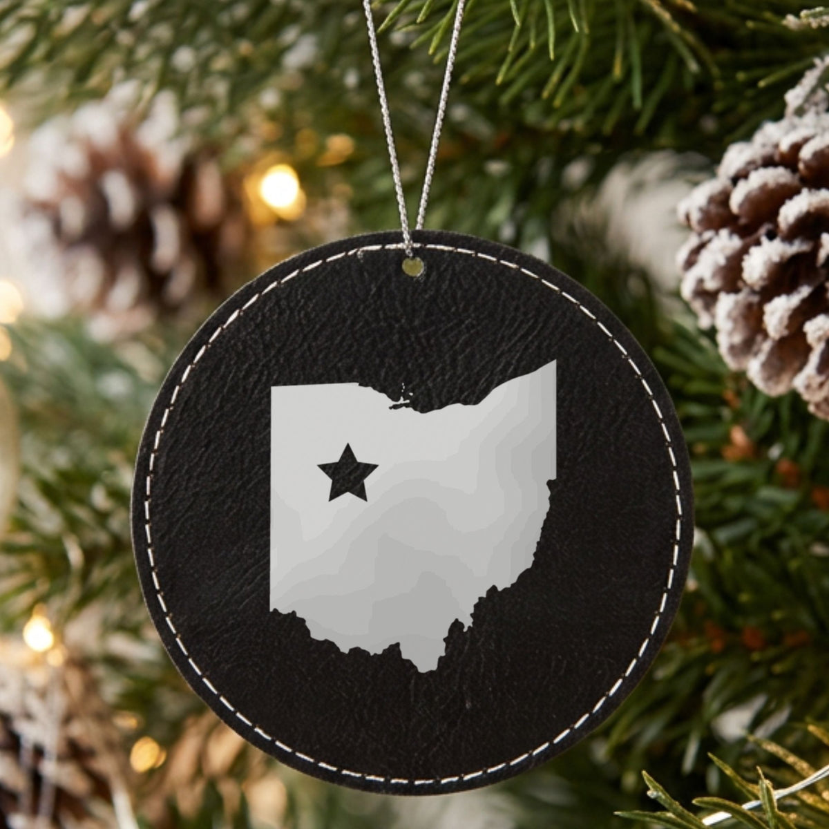 Black leatherette round Christmas ornament laser engraved with the Ohio Star Accent design, hanging on a tree