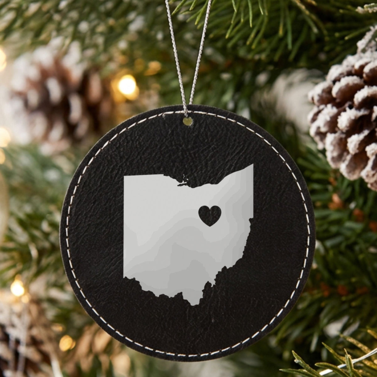Black leatherette round Christmas ornament laser engraved with the Ohio Heart Accent design, hanging on a tree