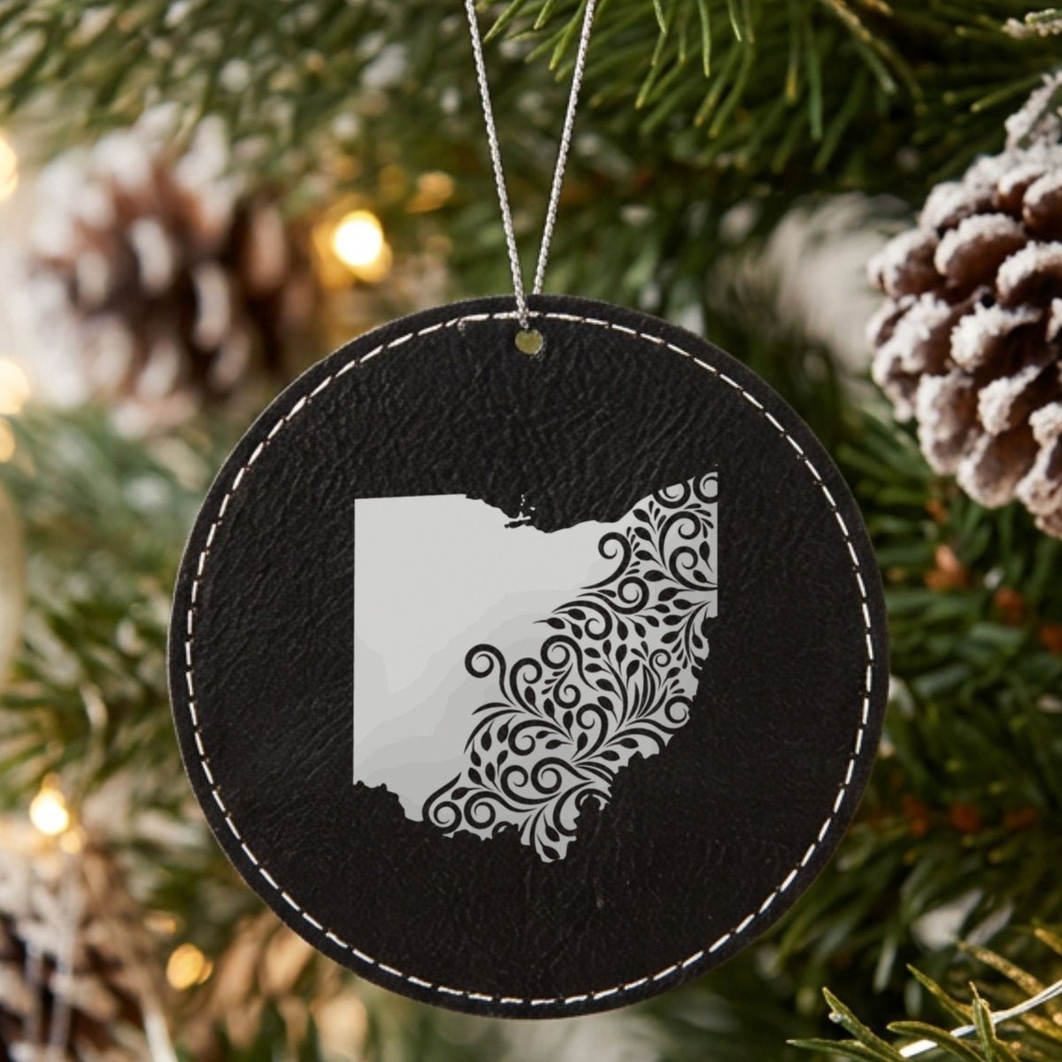 Black leatherette round Christmas ornament laser engraved with the Ohio Floral Damask design, hanging on a tree