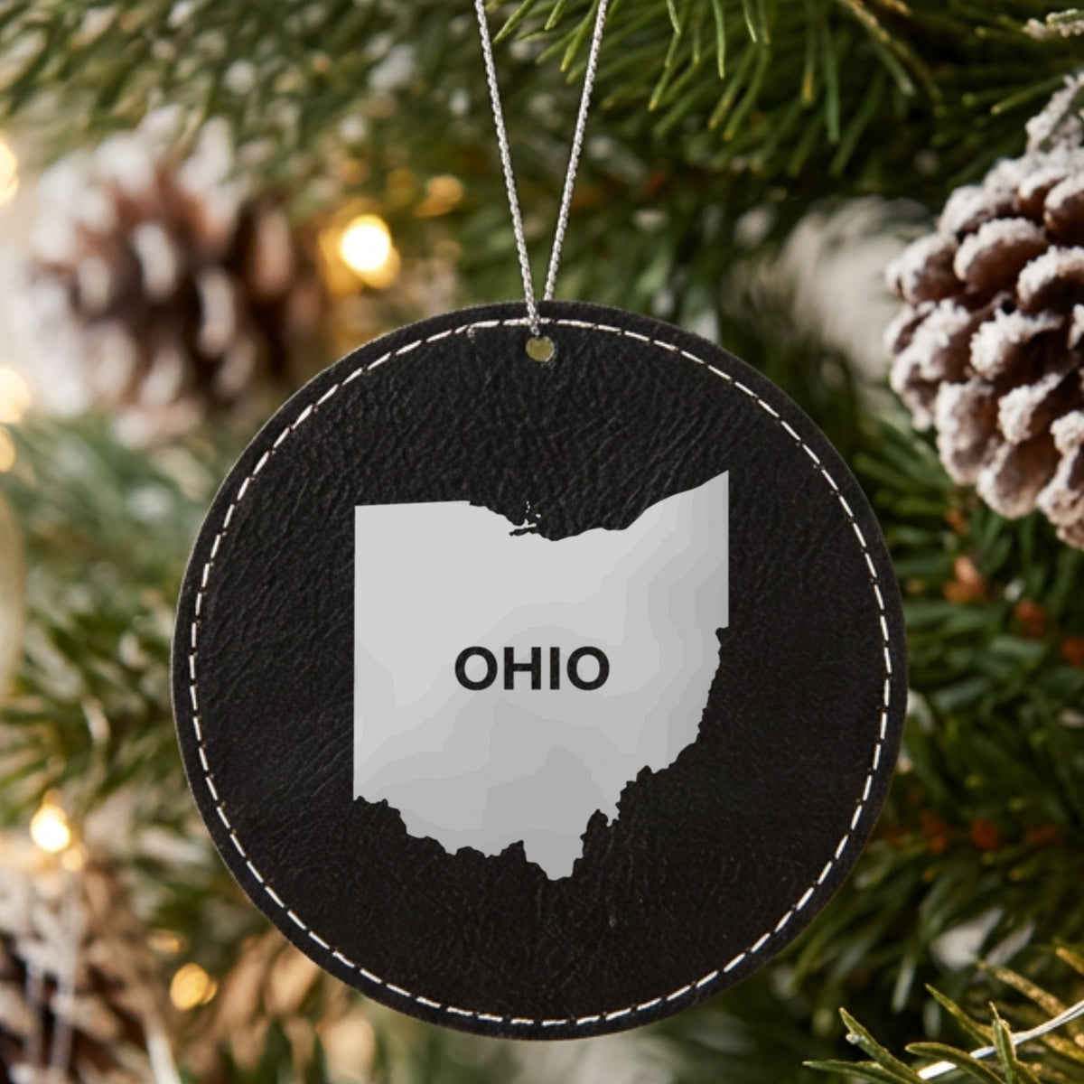 Black leatherette round Christmas ornament laser engraved with the Ohio Bold State Name design, hanging on a tree