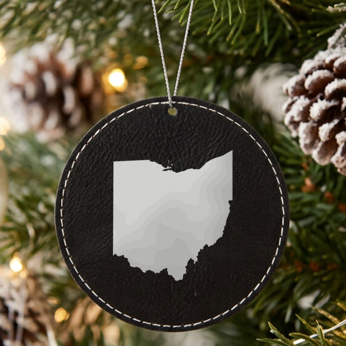 Black leatherette round Christmas ornament laser engraved with the Ohio Engraved State design, hanging on a tree