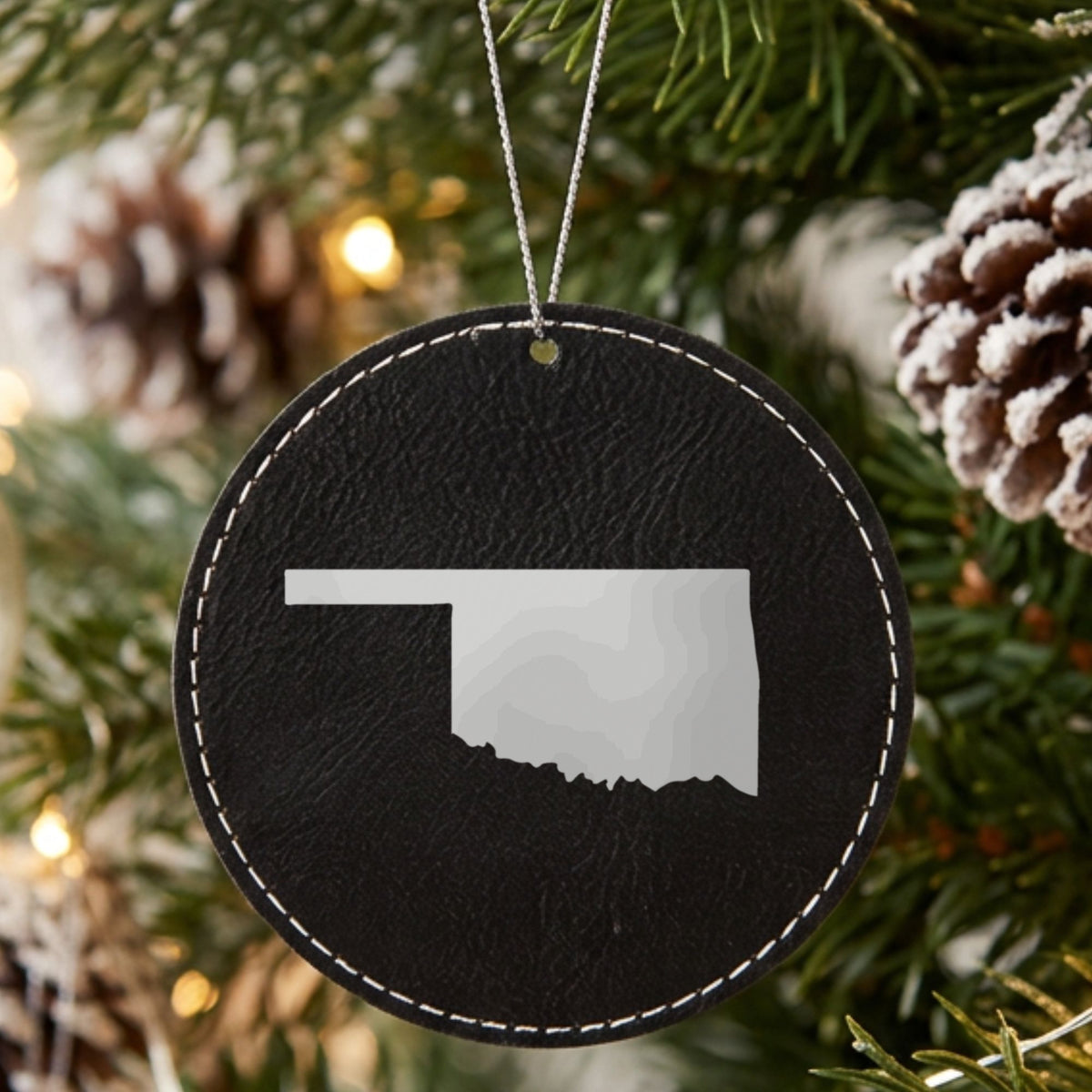 Black leatherette round Christmas ornament laser engraved with the Oklahoma Engraved State design, hanging on a tree