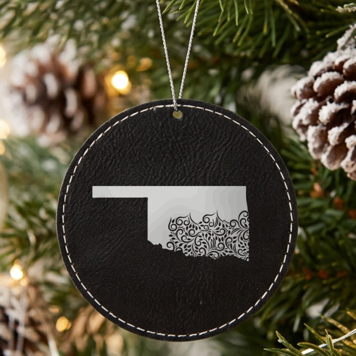 Black leatherette round Christmas ornament laser engraved with the Oklahoma Floral Damask design, hanging on a tree