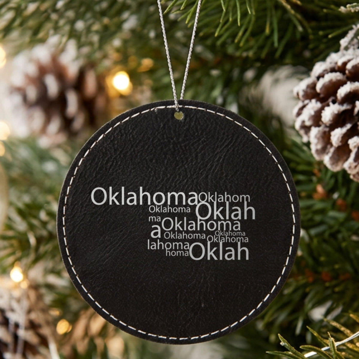 Black leatherette round Christmas ornament laser engraved with the Oklahoma Word Cloud design, hanging on a tree