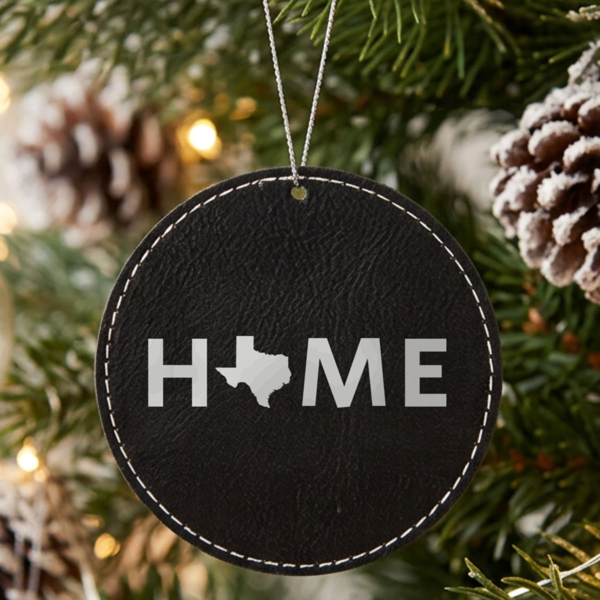Black leatherette round Christmas ornament laser engraved with the Texas HOME Outline design, hanging on a tree