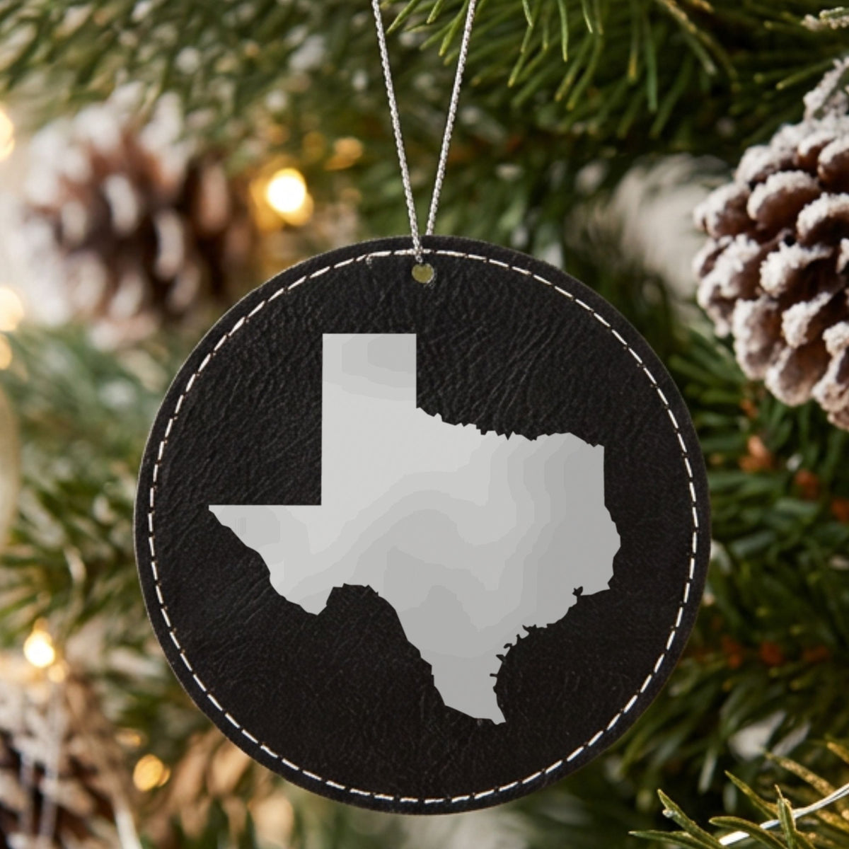 Black leatherette round Christmas ornament laser engraved with the Texas Engraved State design, hanging on a tree
