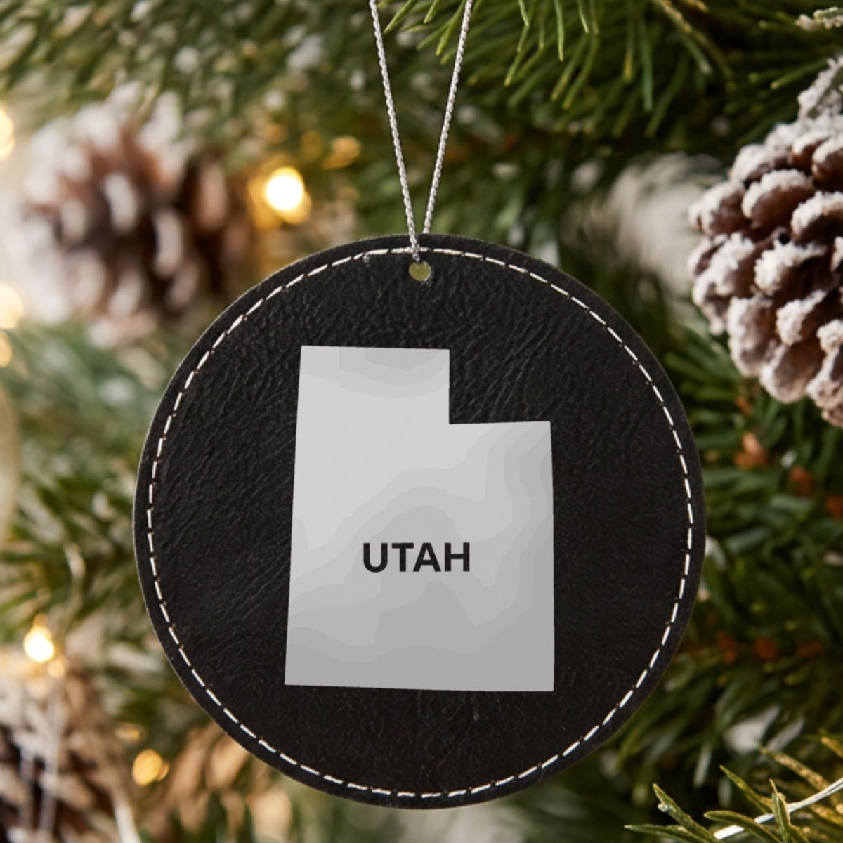 Black leatherette round Christmas ornament laser engraved with the Utah Bold State Name design, hanging on a tree