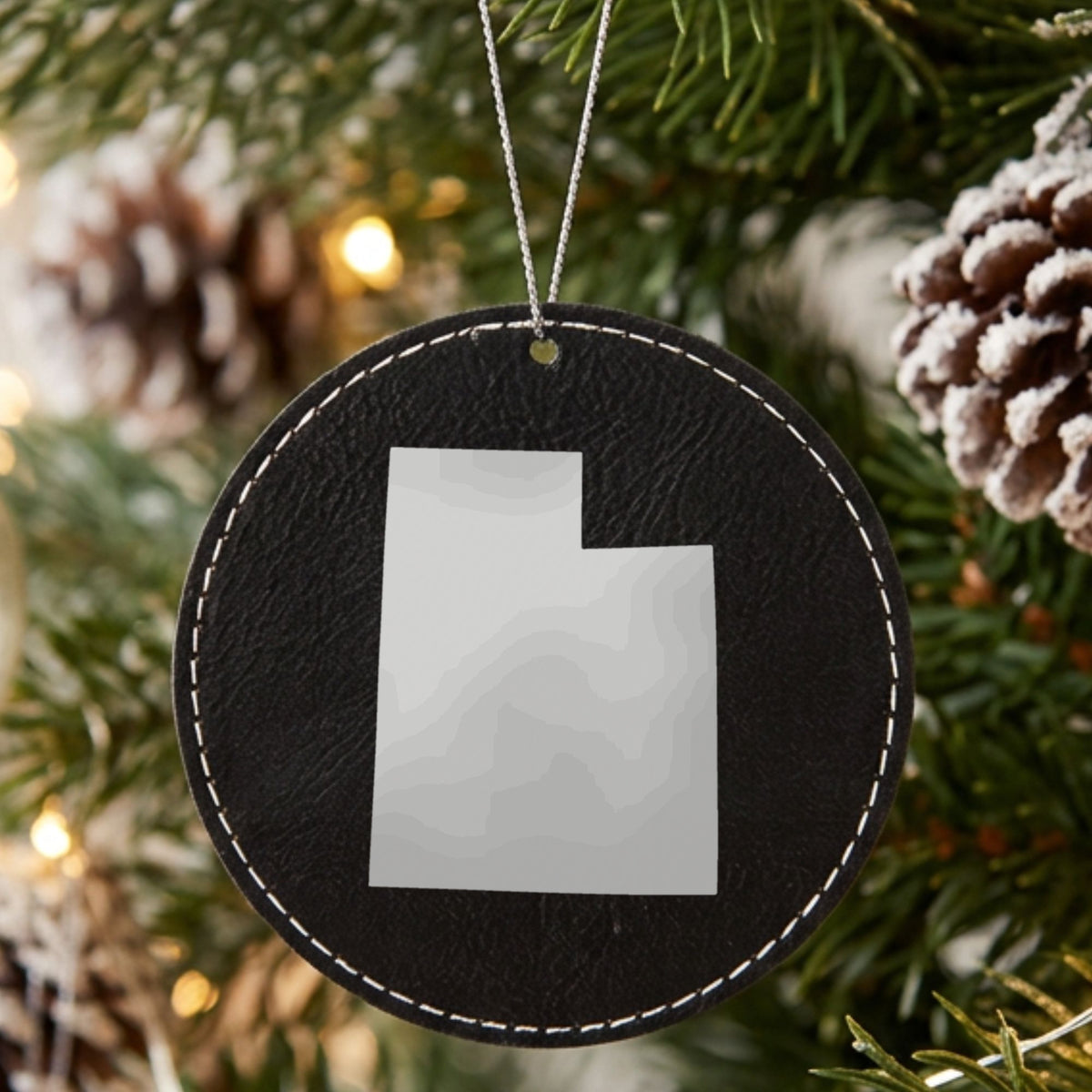 Black leatherette round Christmas ornament laser engraved with the Utah Engraved State design, hanging on a tree