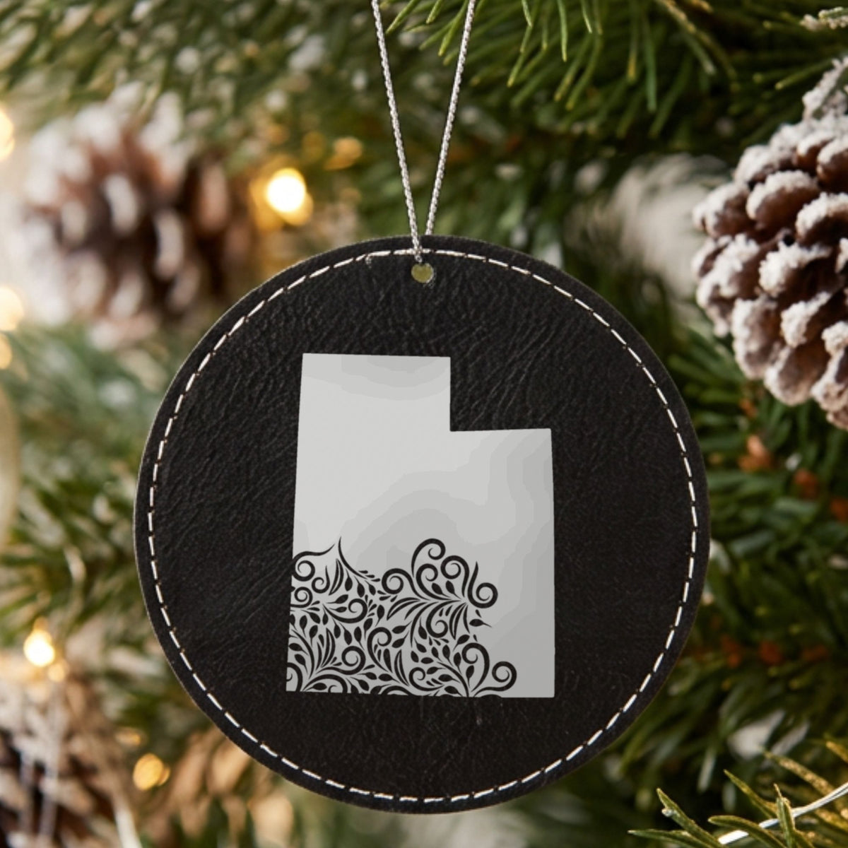 Black leatherette round Christmas ornament laser engraved with the Utah Floral Damask design, hanging on a tree