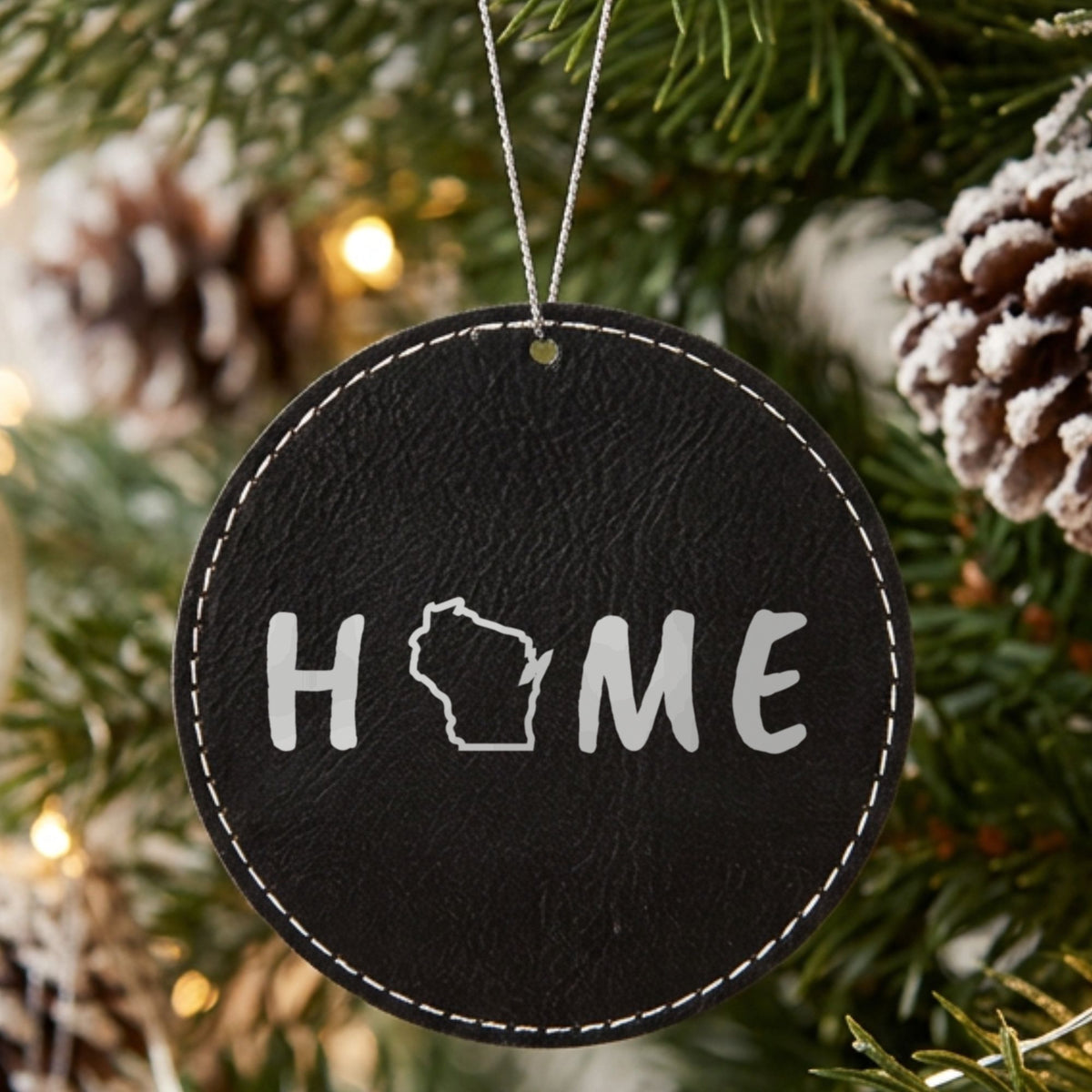 Black leatherette round Christmas ornament laser engraved with the Wisconsin HOME Outline design, hanging on a tree
